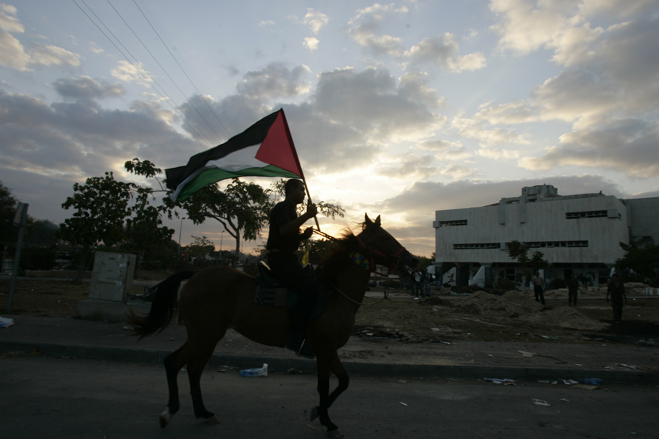 A Palestinian rides his horse while holding a Palestinian flag as he passes a synagogue in Neve Dekalim.