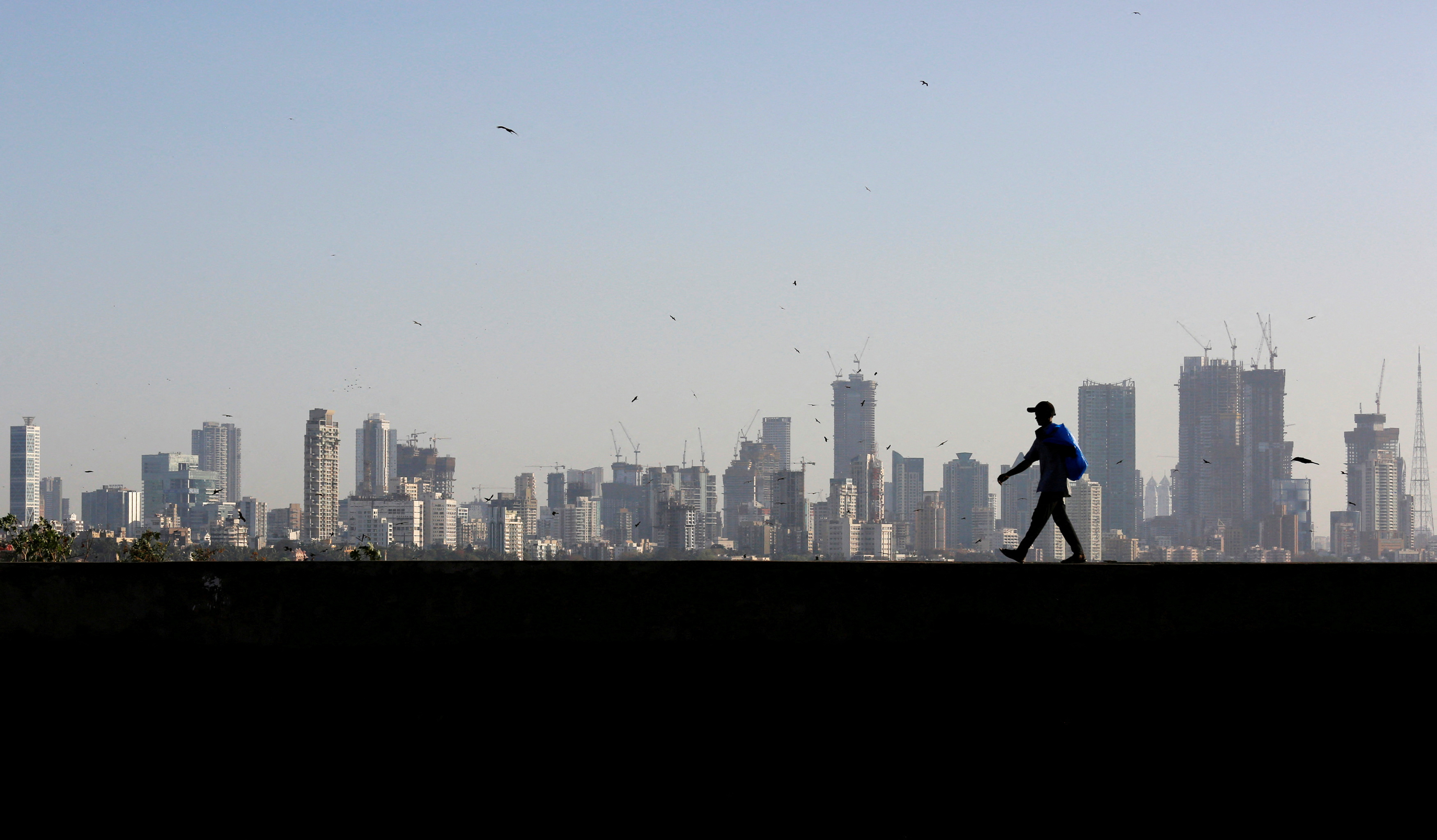 A man walks along a wall overlooking the central Mumbai's financial district skyline