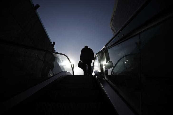 Man holding a briefcase rides up an escalator at a subway station on a cold but sunny day in central Seoul