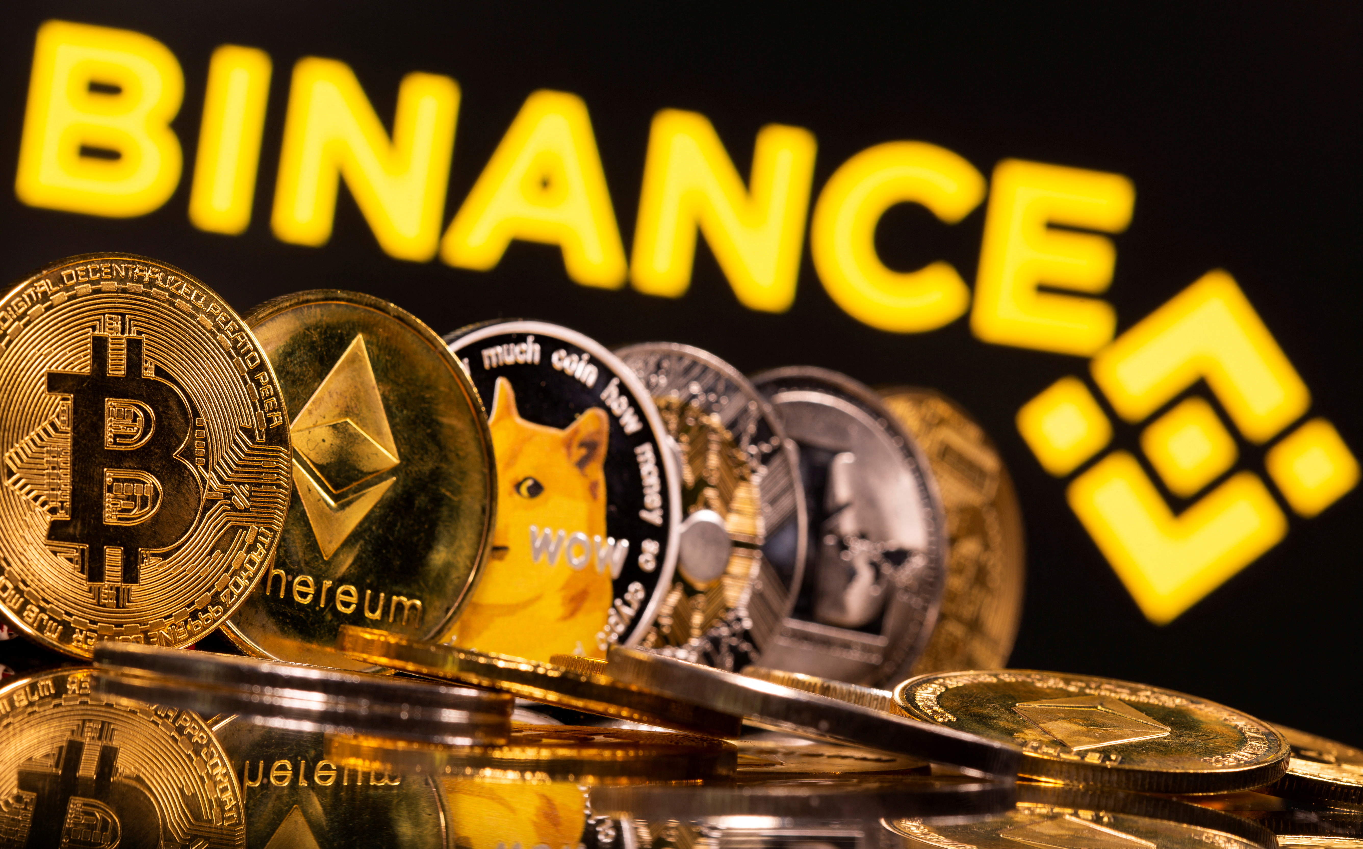 Representations of cryptocurrencies Bitcoin, Ethereum, DogeCoin, Ripple, and Litecoin are seen in front of a displayed Binance logo