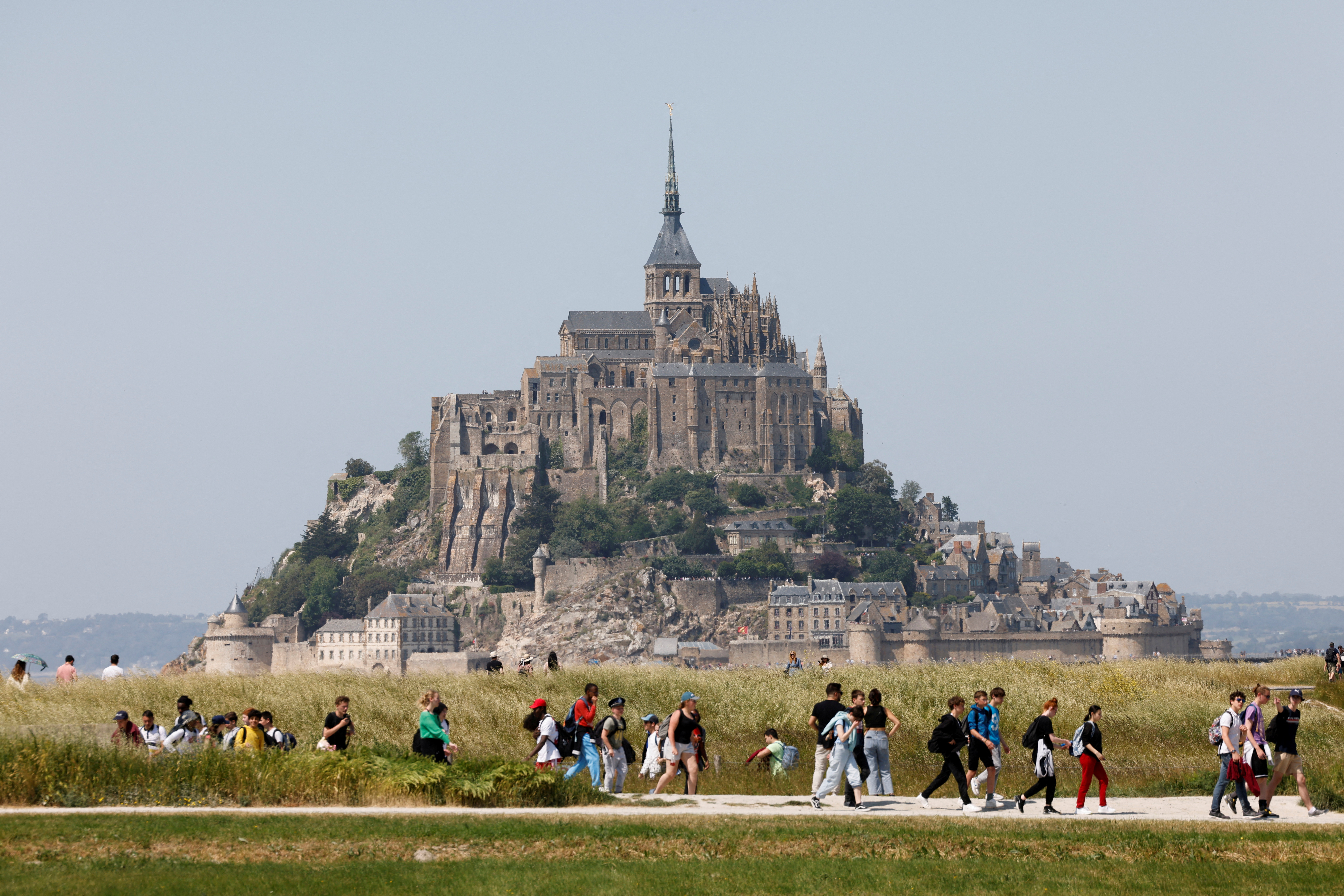 People walk past France's Mont-Saint-Michel during the French President's two-day visit in Normandy, in Le Mont-Saint-Michel