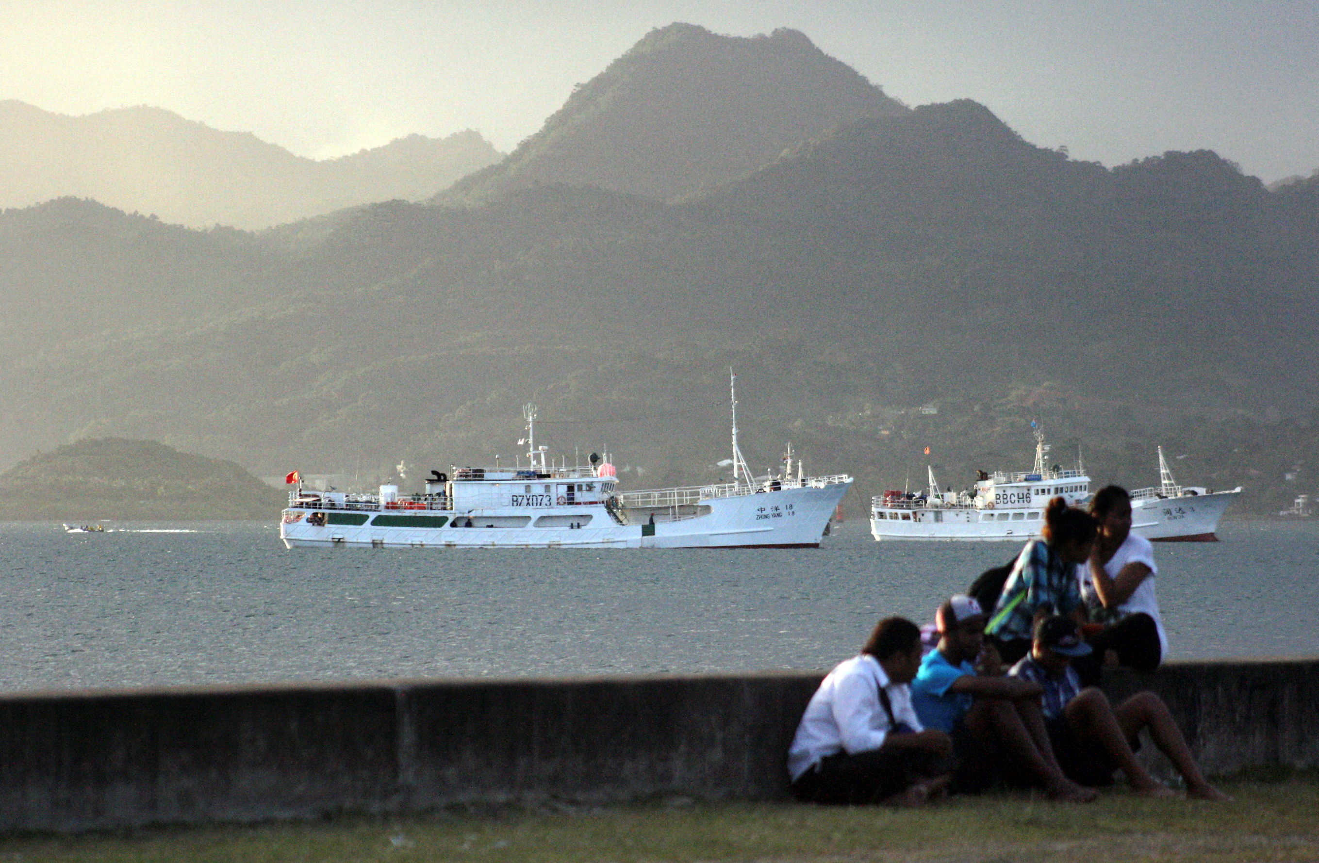Locals sit on a wall situated on the foreshore of the harbour in the Fiji capital of Suva