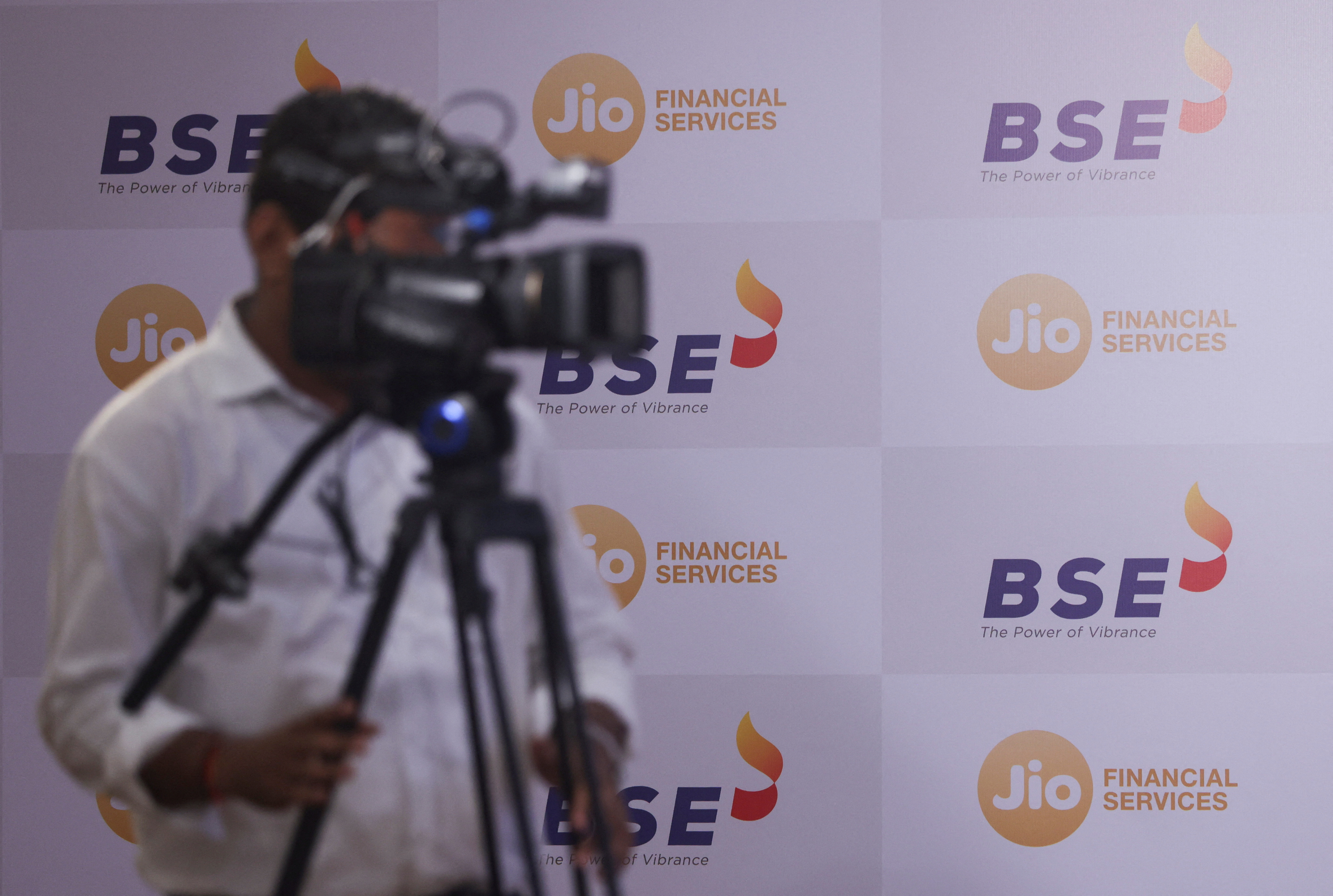 A cameraman is seen next to logos of Jio Financial Services and Bombay Stock Exchange ahead of its listing ceremony at the Bombay Stock Exchange in Mumbai