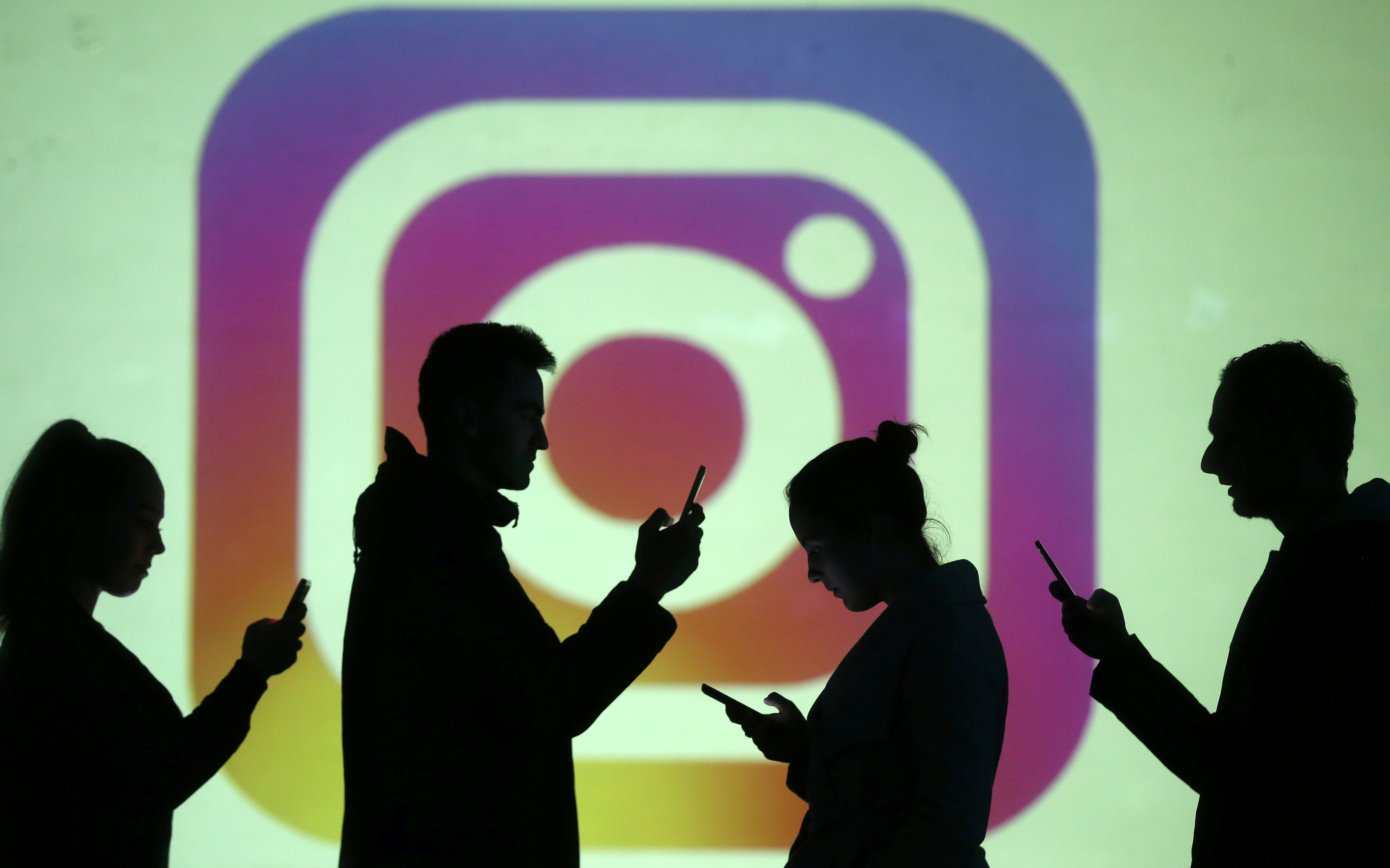 Silhouettes of mobile users are seen next to a screen projection of Instagram logo in this picture illustration taken March 28, 2018.  REUTERS/Dado Ruvic/Illustration