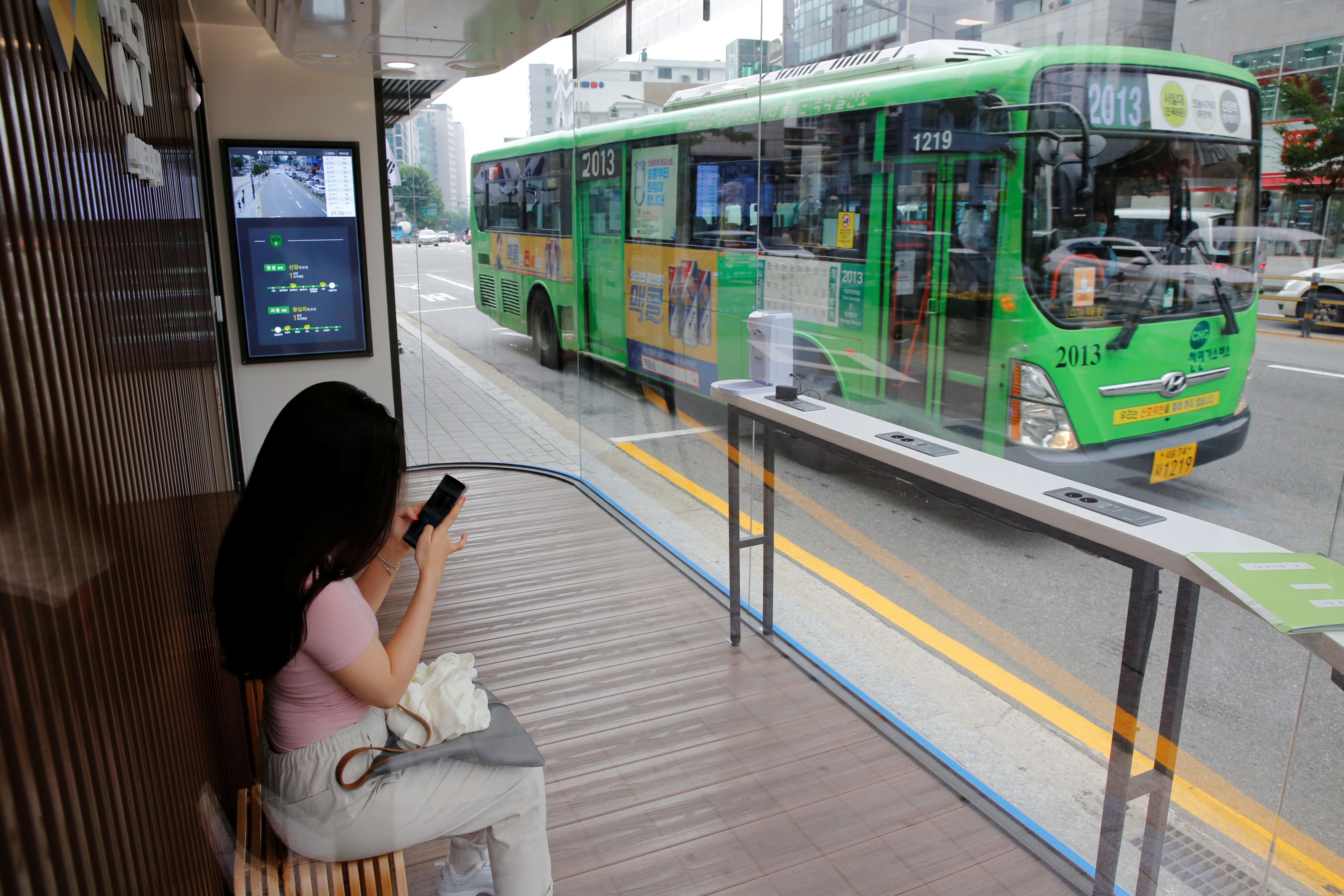Woman waits for a bus inside a glass-covered bus stop in Seoul