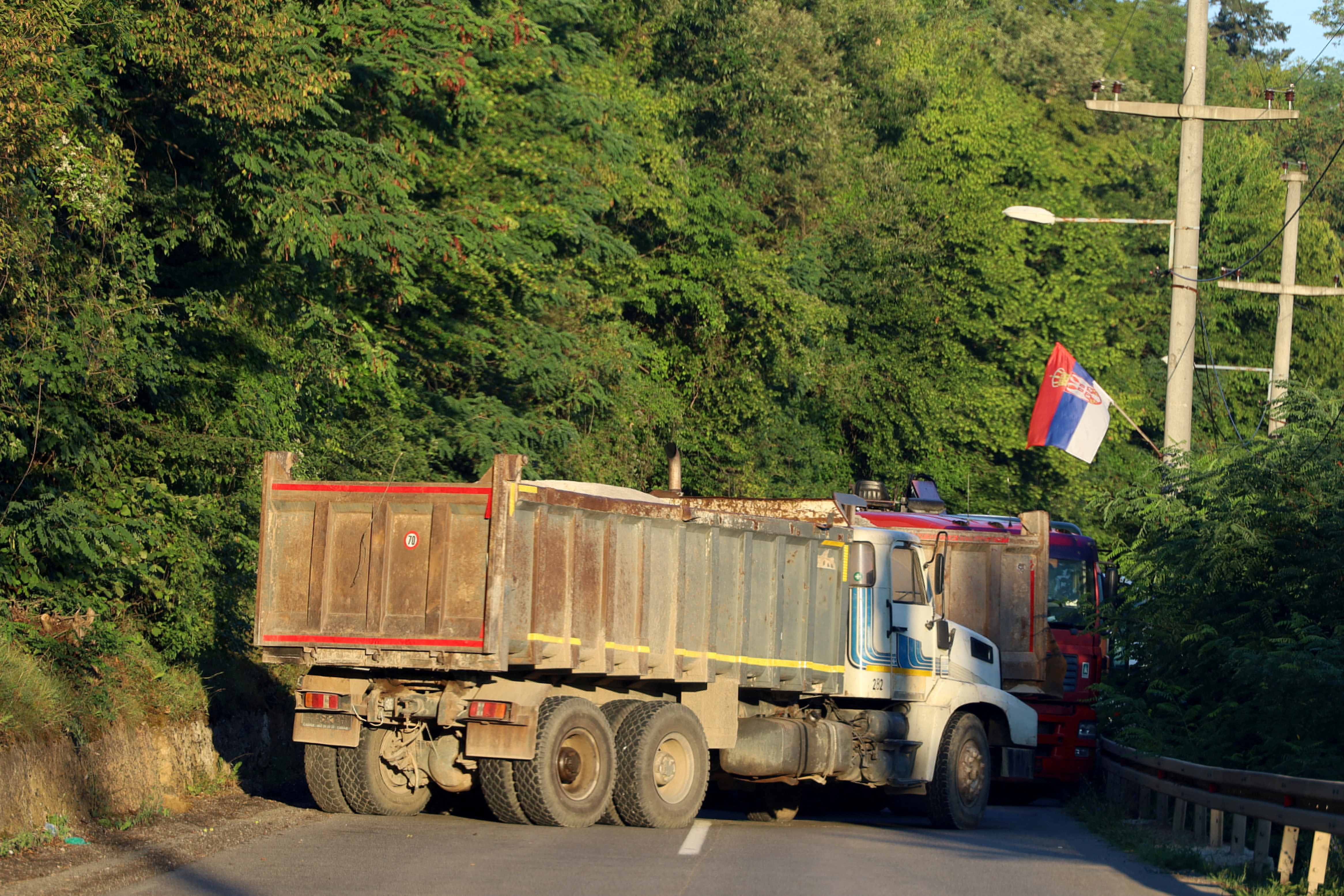 A Serbian flag is seen as trucks block a road in Zupce