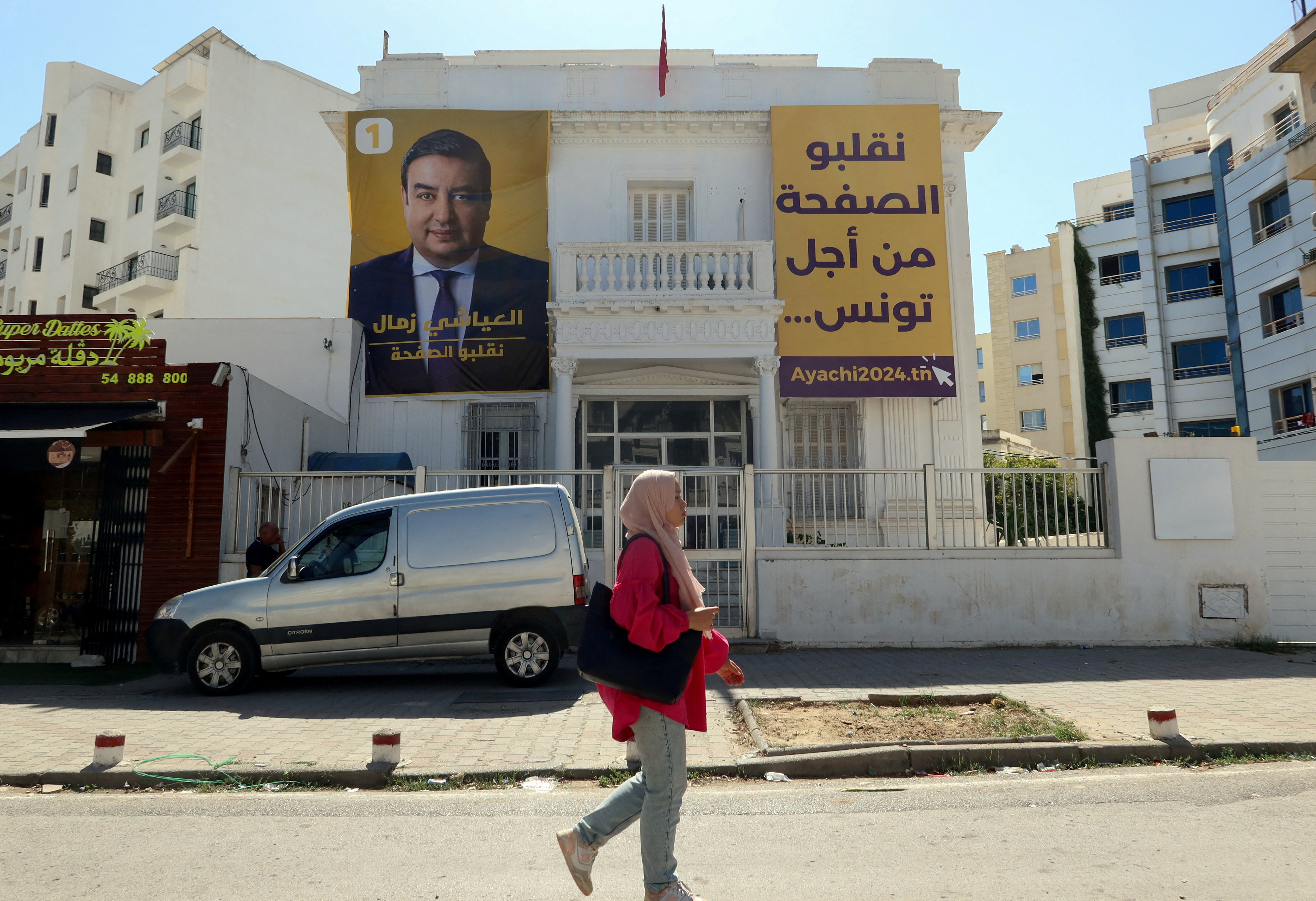 A woman walks past a poster depicting presidential candidate Ayachi Zammel, hanging on his party's Azimoun headquarters in Tunis