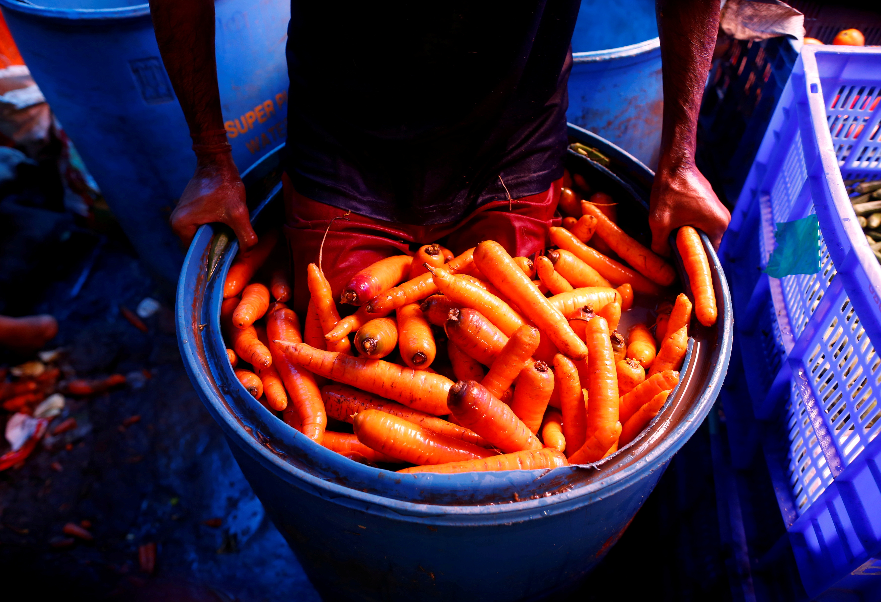 A worker washes carrots in a plastic drum at a wholesale vegetable market in Mumbai