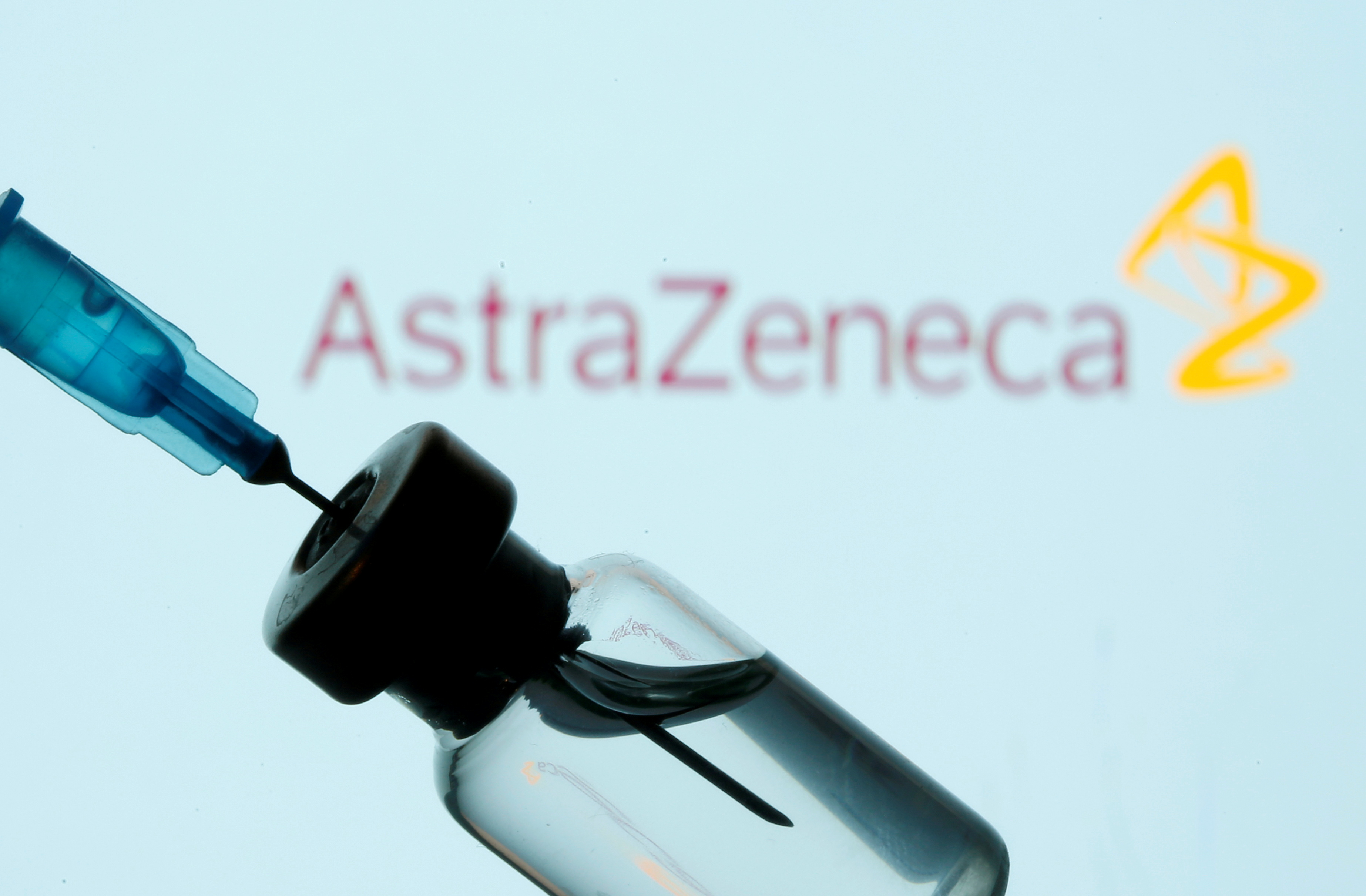 Vial and sryinge are seen in front of displayed AstraZeneca logo