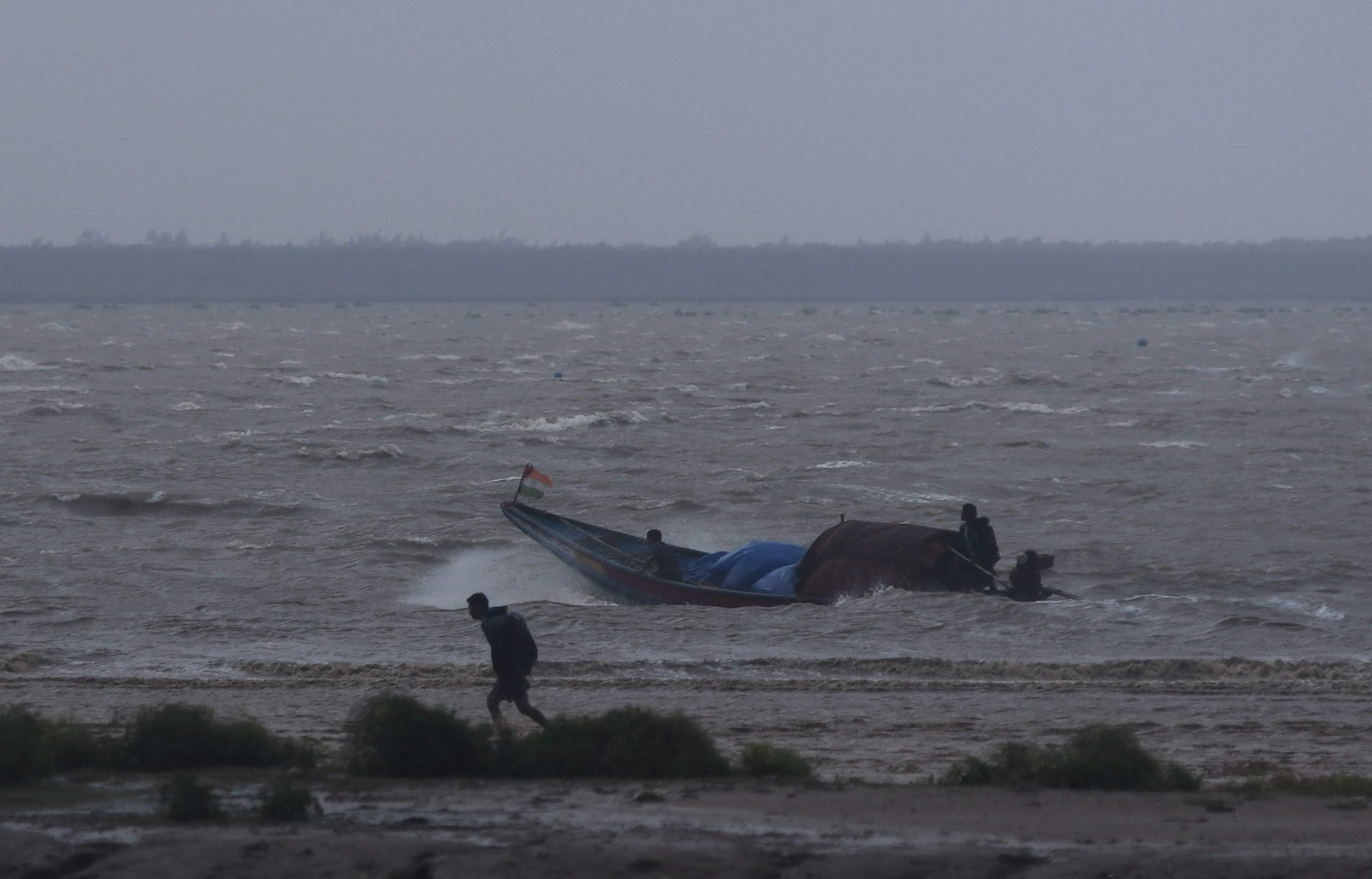 Fishermen attempt to bring their boat back to shore during high tide before Cyclone Dana makes landfall, in Odisha