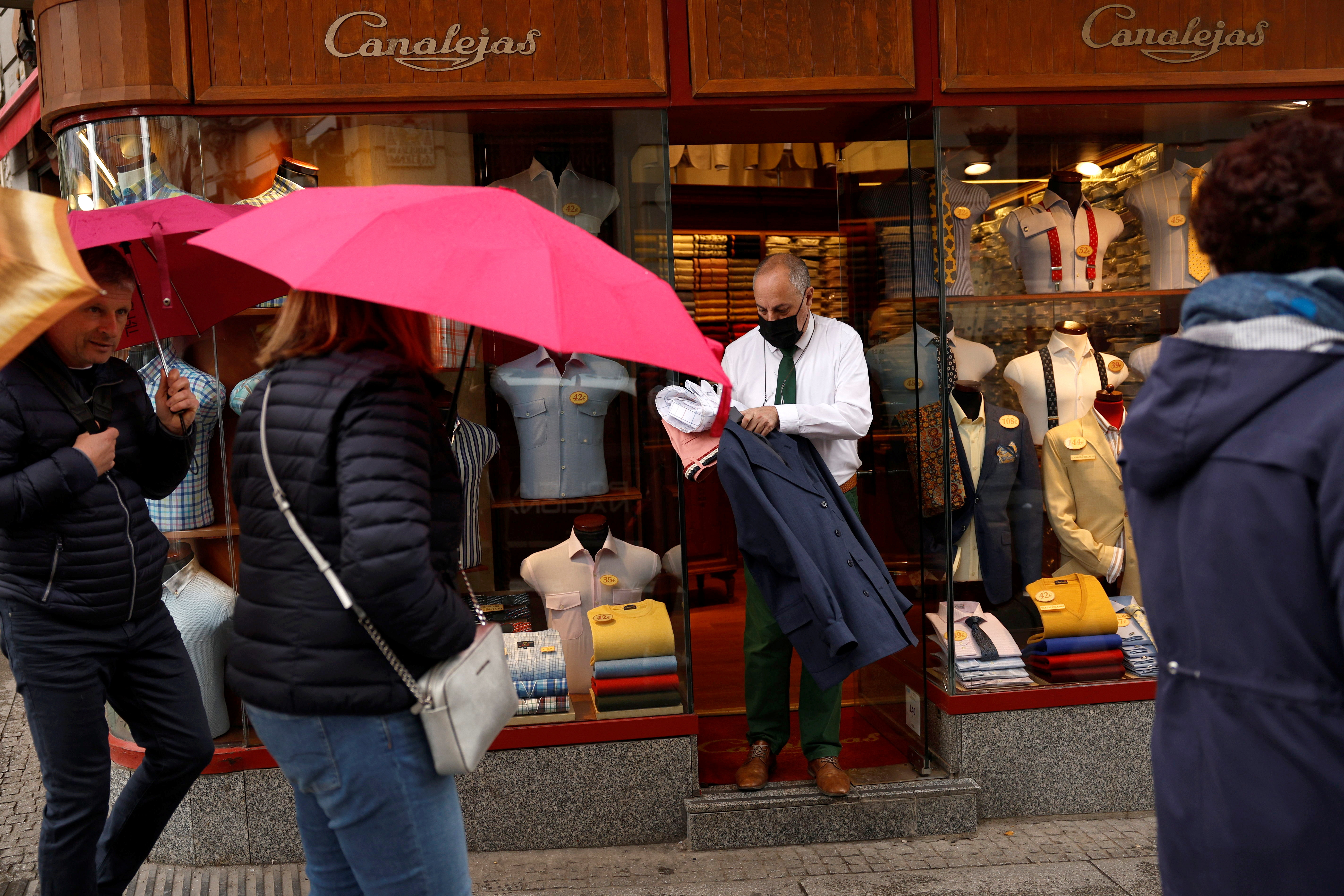 A shirt maker holds clothes at the entrance to a shirt and clothing store in central Madrid