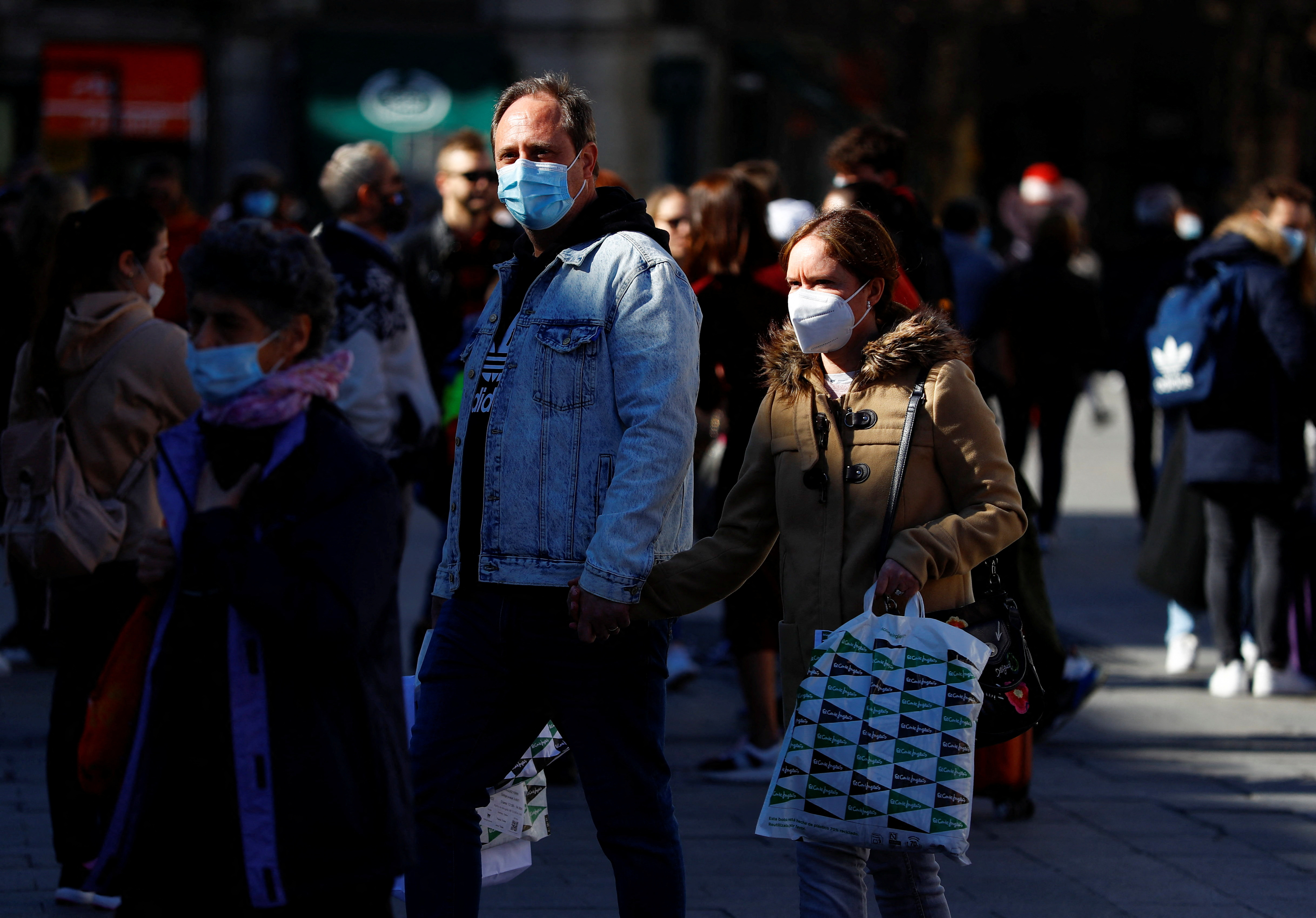People wearing protective face masks walk down a street in Madrid