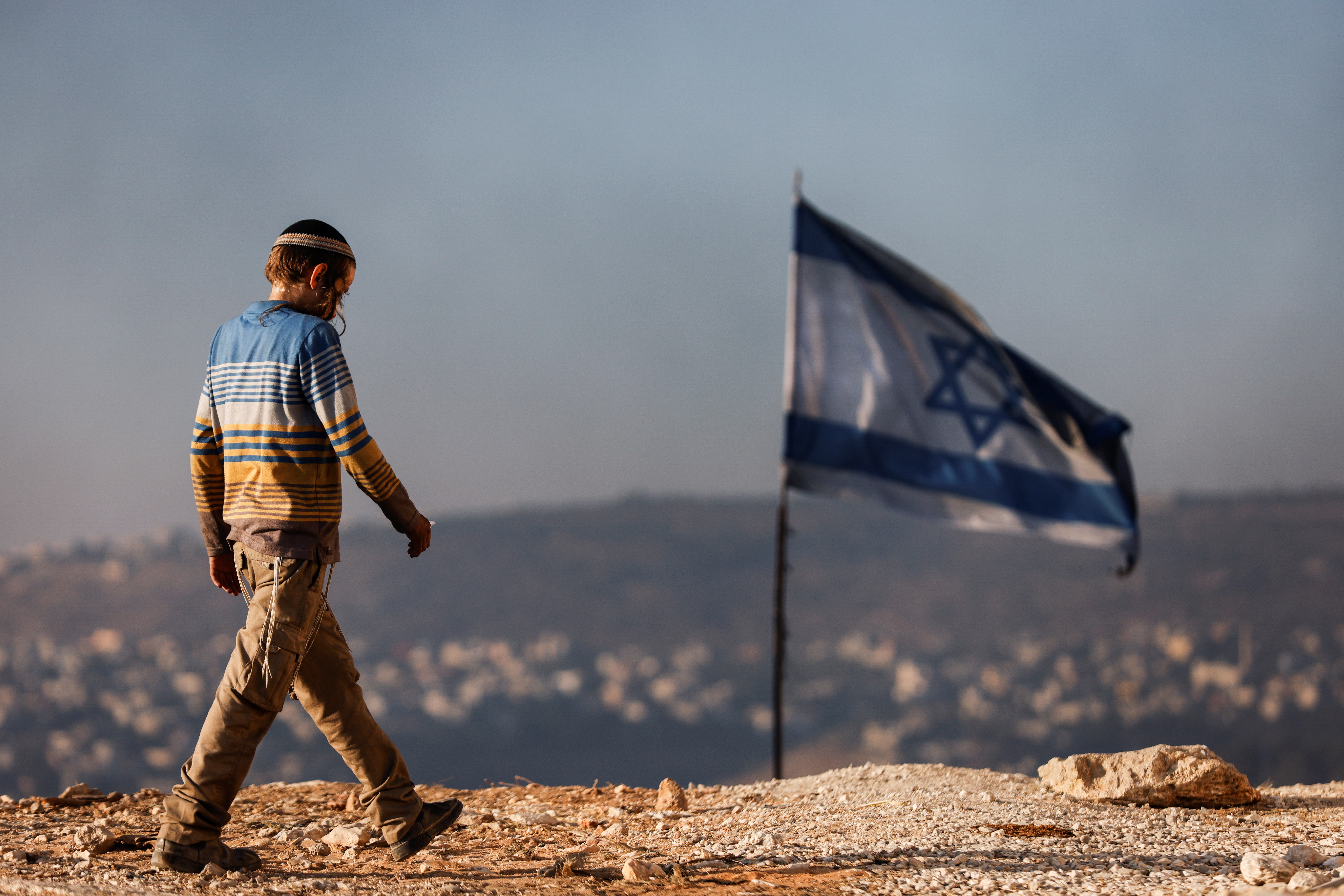 A Jewish settler teenager walks by an Israeli flag in Givat Eviatar, a new Israeli settler outpost, near the Palestinian village of Beita in the Israeli-occupied West Bank