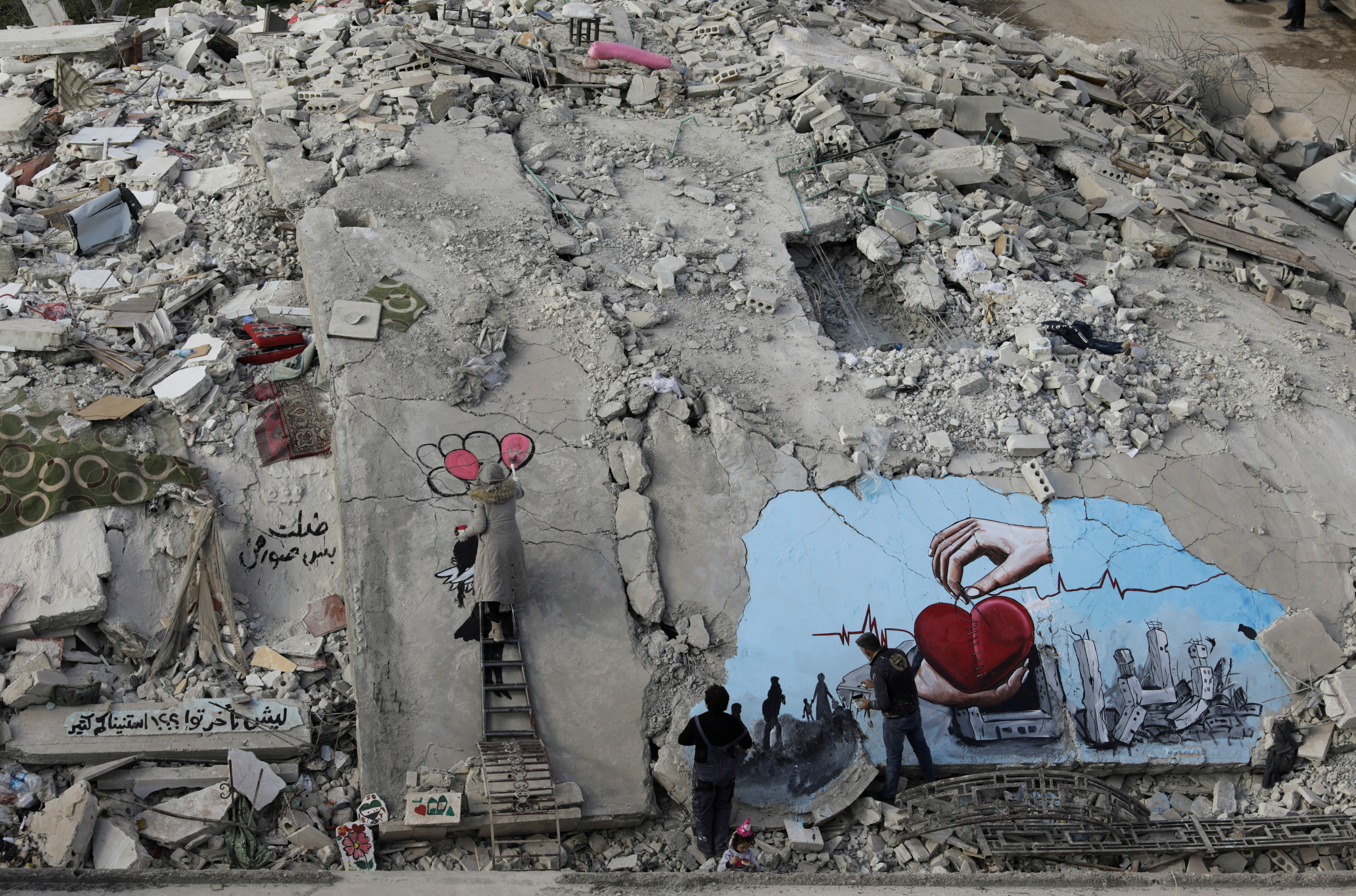 Syrian artists Aziz Asmar and Salam Hamed paint street art on rubble of damaged buildings in the rebel-held town of Jandaris