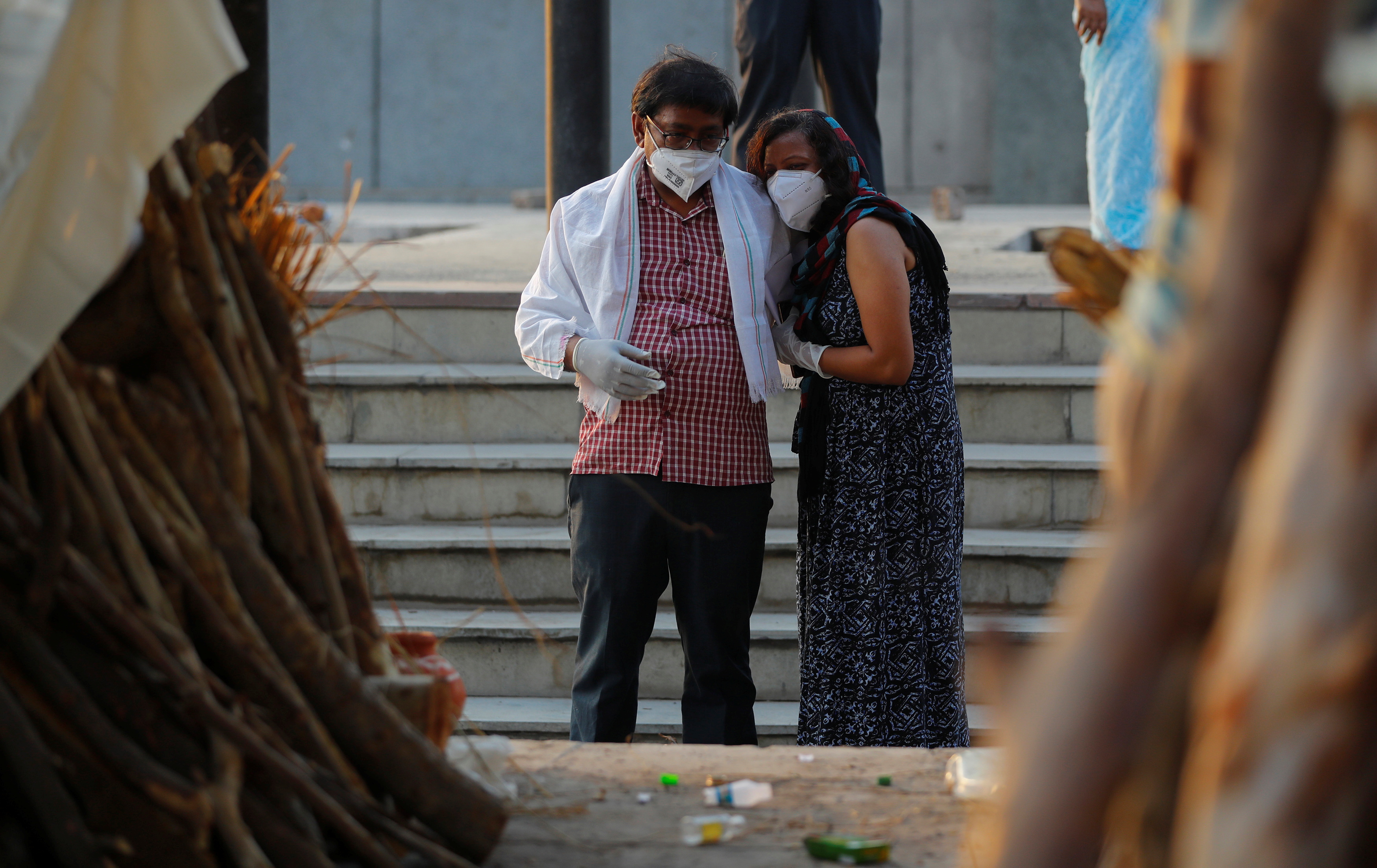 A couple mourns as they stand next to the funeral pyre of a relative who died due to the coronavirus disease (COVID-19), at a crematorium in New Delhi