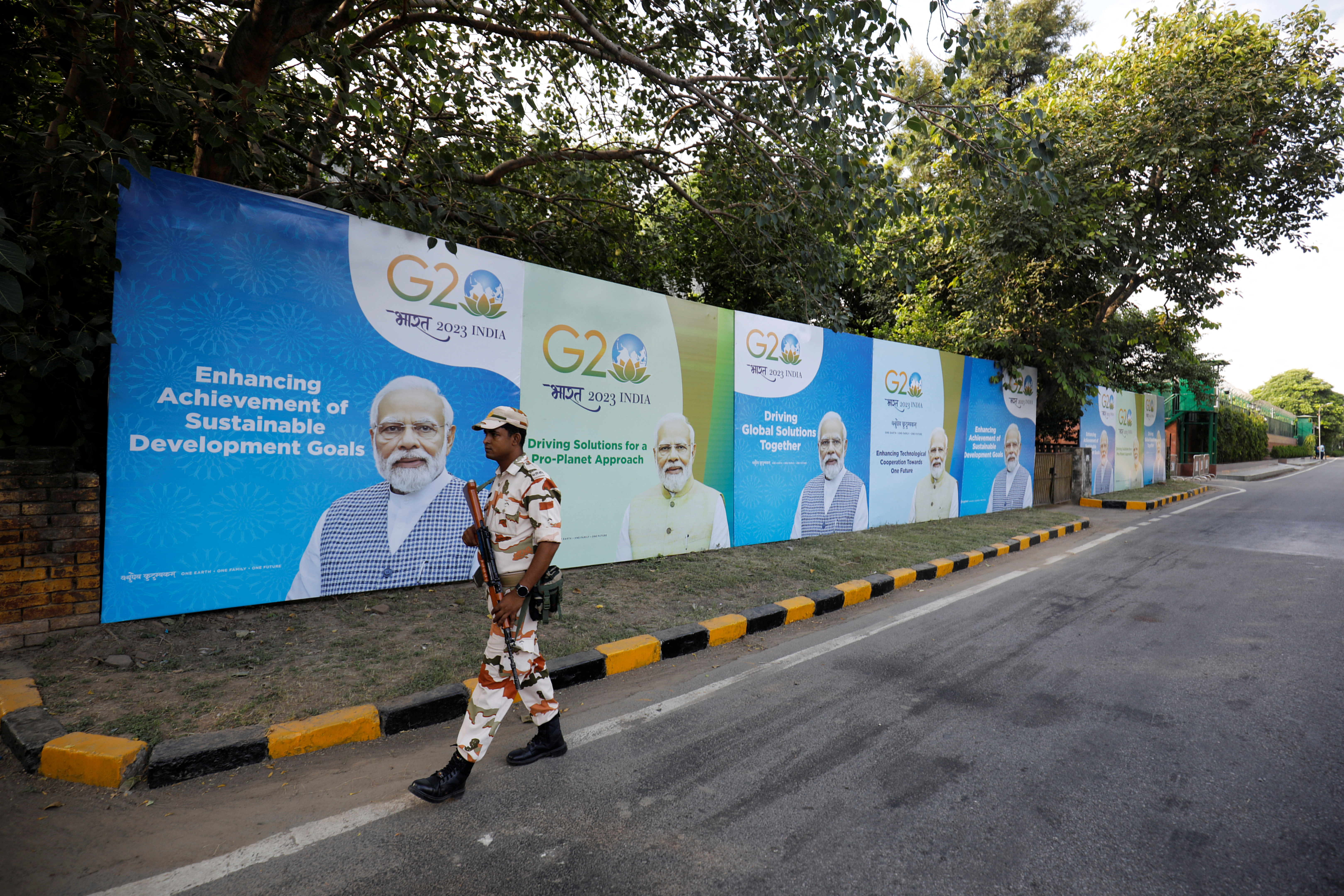 A security force personnel patrols past hoardings featuring India's PM Modi along an empty road ahead of the G20 Summit in New Delhi