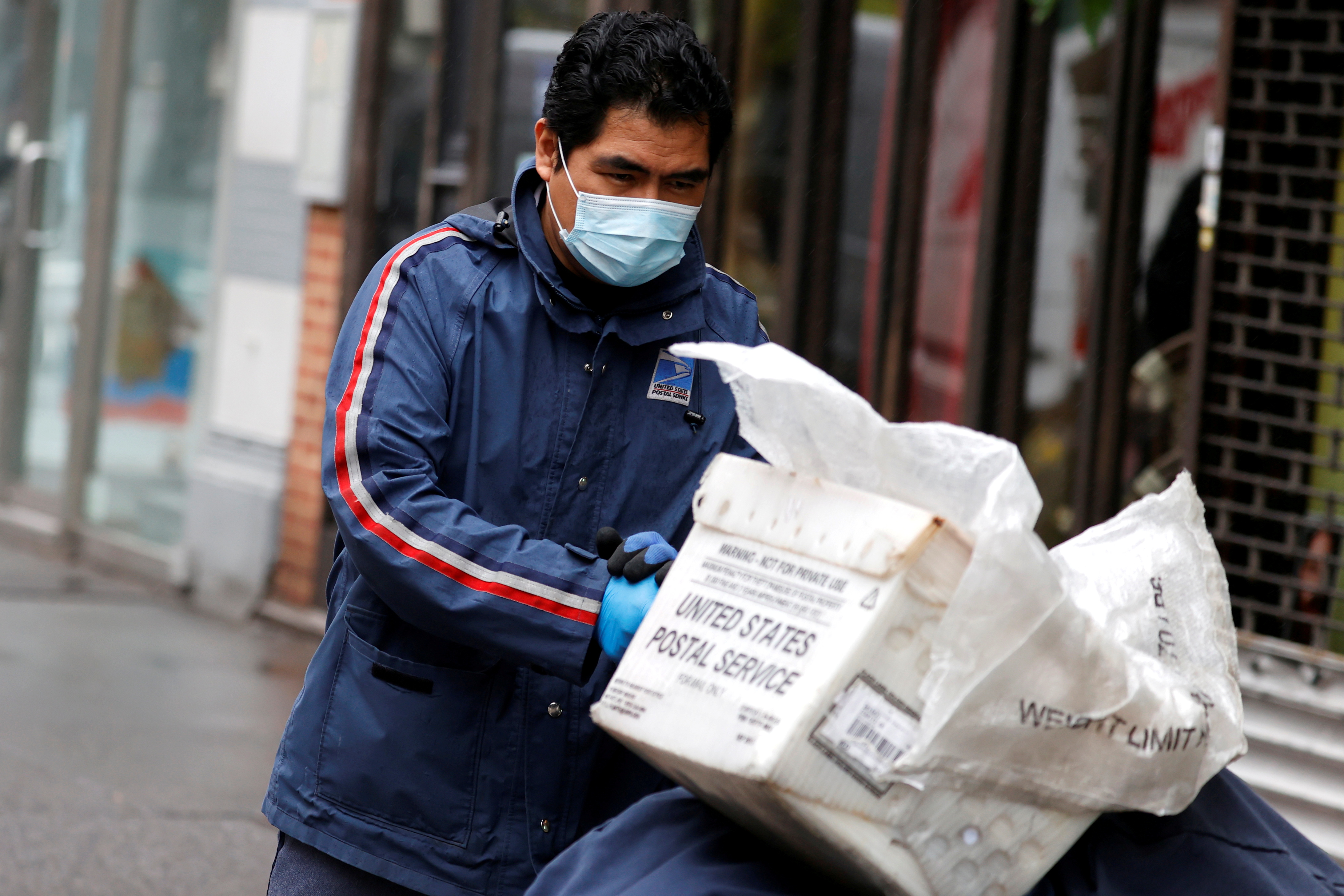 A United States Postal Service (USPS) mail carrier pushes his cart while delivering mail in the rain on Manhattan's Upper West Side during the outbreak of the coronavirus disease (COVID-19) in New York City, New York, U.S., April 13, 2020. REUTERS/Mike Segar/File Photo