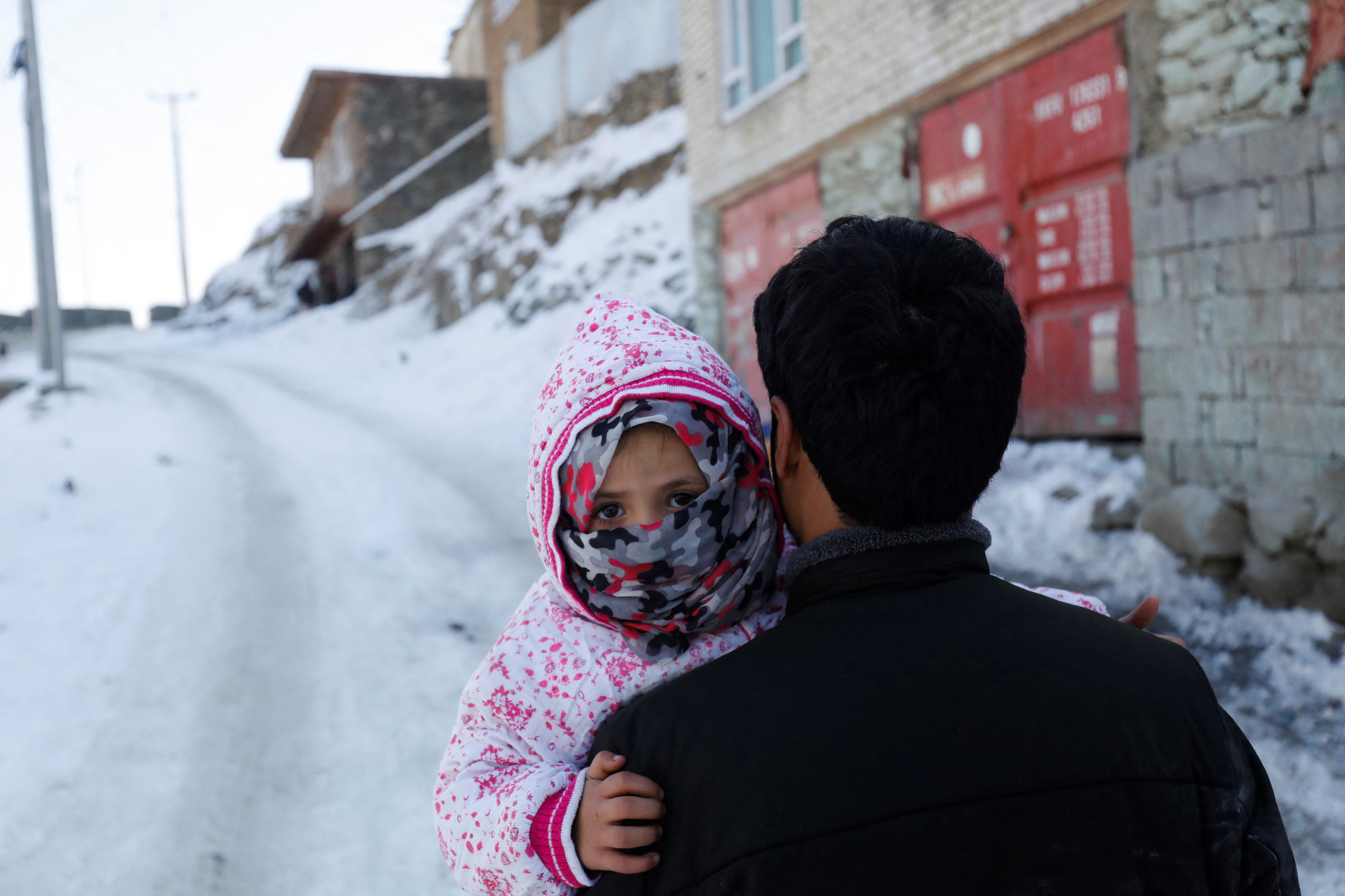 An Afghan man holds his child as he walks on a snow-covered street on the TV mountain in Kabul
