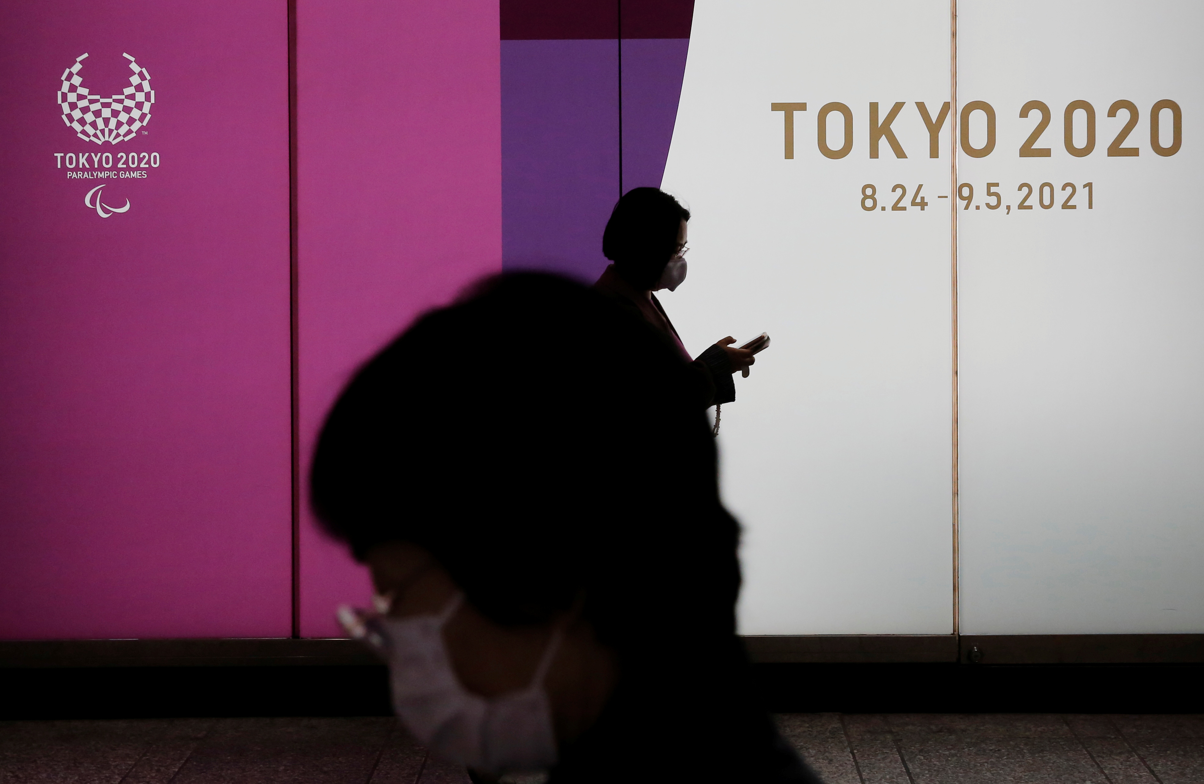 Women walk past a promotional board for 2020 Tokyo Olympic Games, in Tokyo