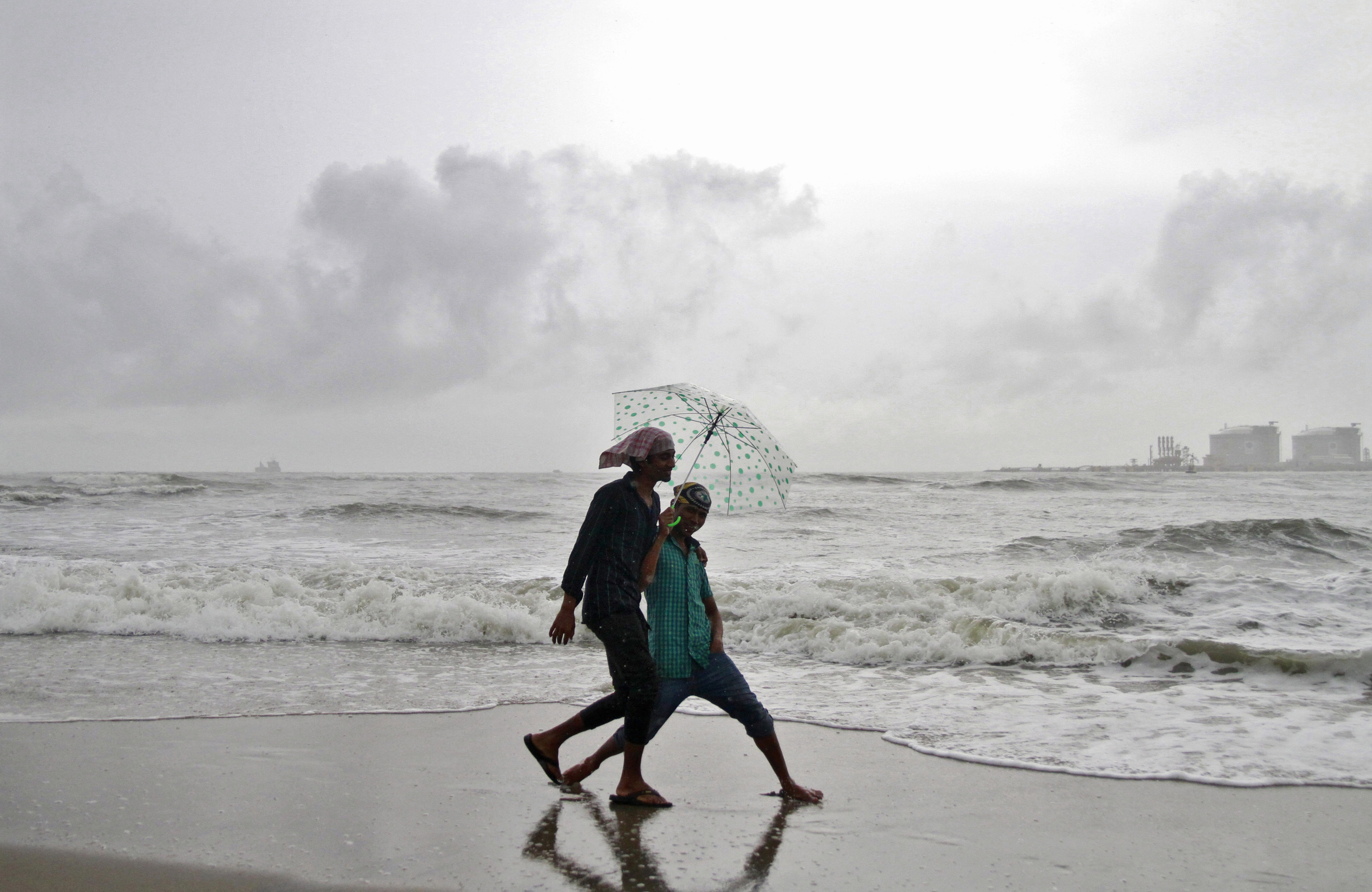 Beachgoers react to the camera while holding an umbrella as it drizzles at the Fort Kochi beach in Kochi