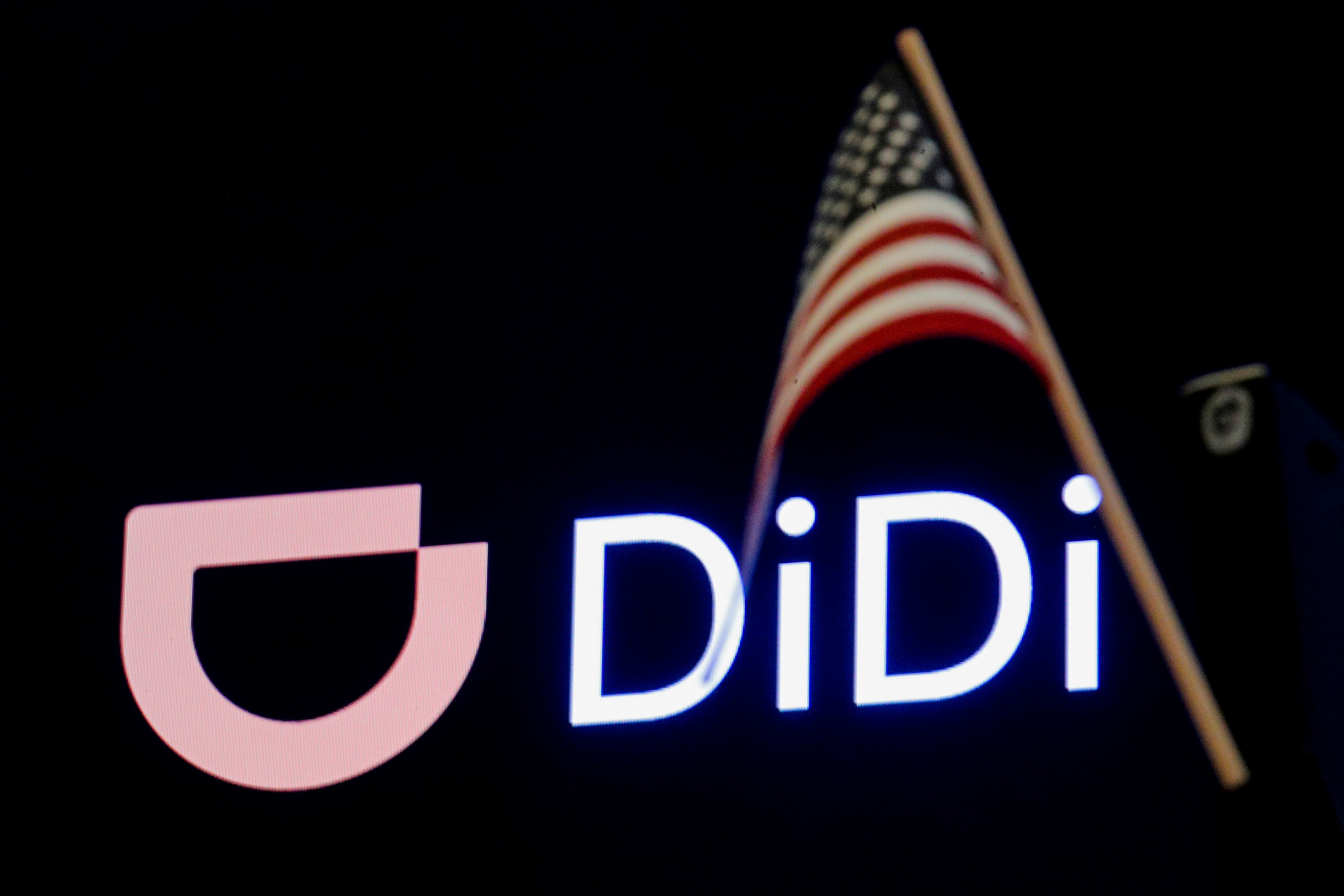 An American flag is pictured in front of the logo for Chinese ride hailing company Didi Global Inc. during the IPO on the New York Stock Exchange (NYSE) floor in New York City, U.S., June 30, 2021. REUTERS/Brendan McDermid/File Photo