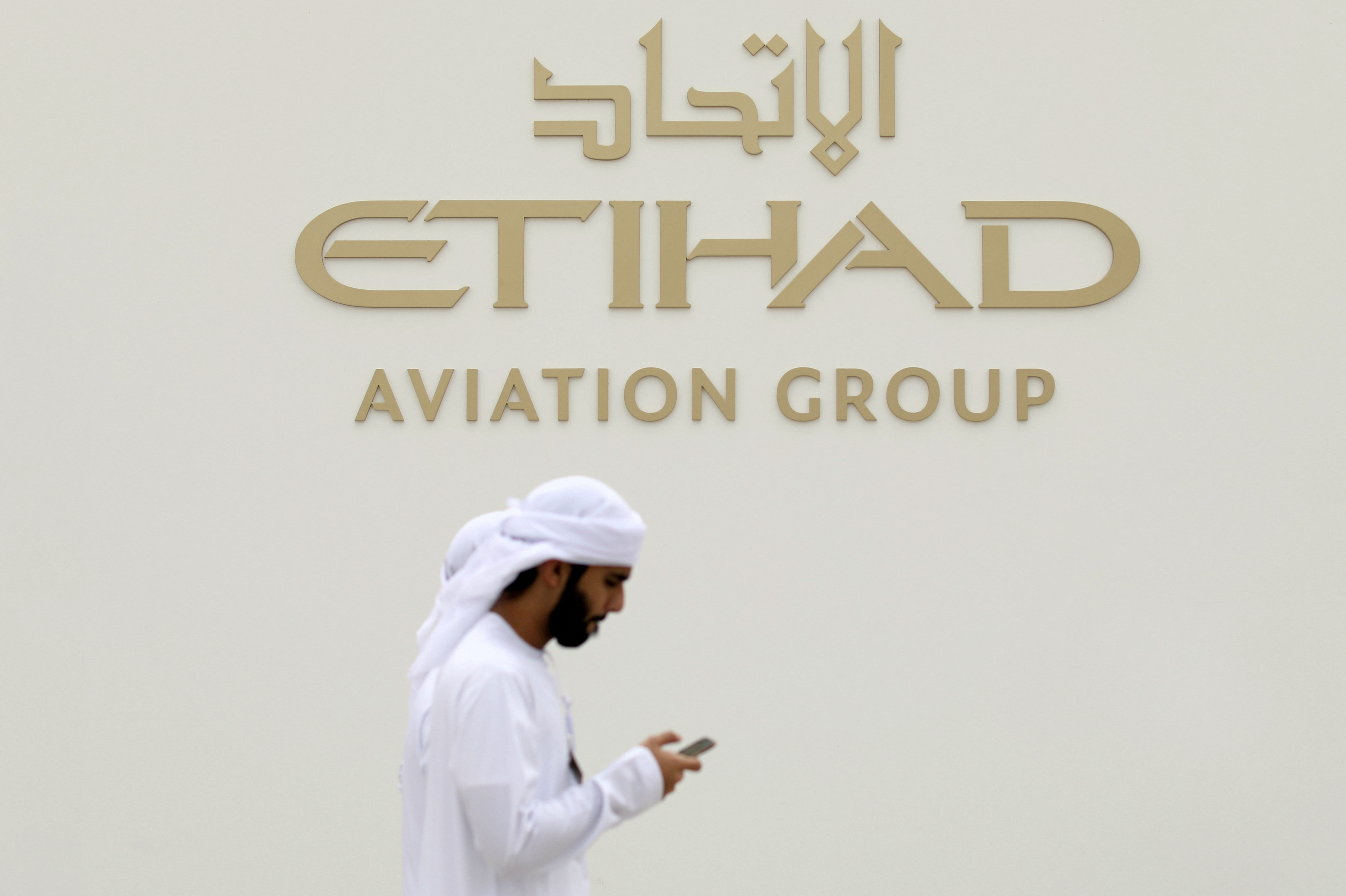 A visitor walks past the Etihad Aviation Group logo on display during the fifth day of Dubai Air Show in Dubai