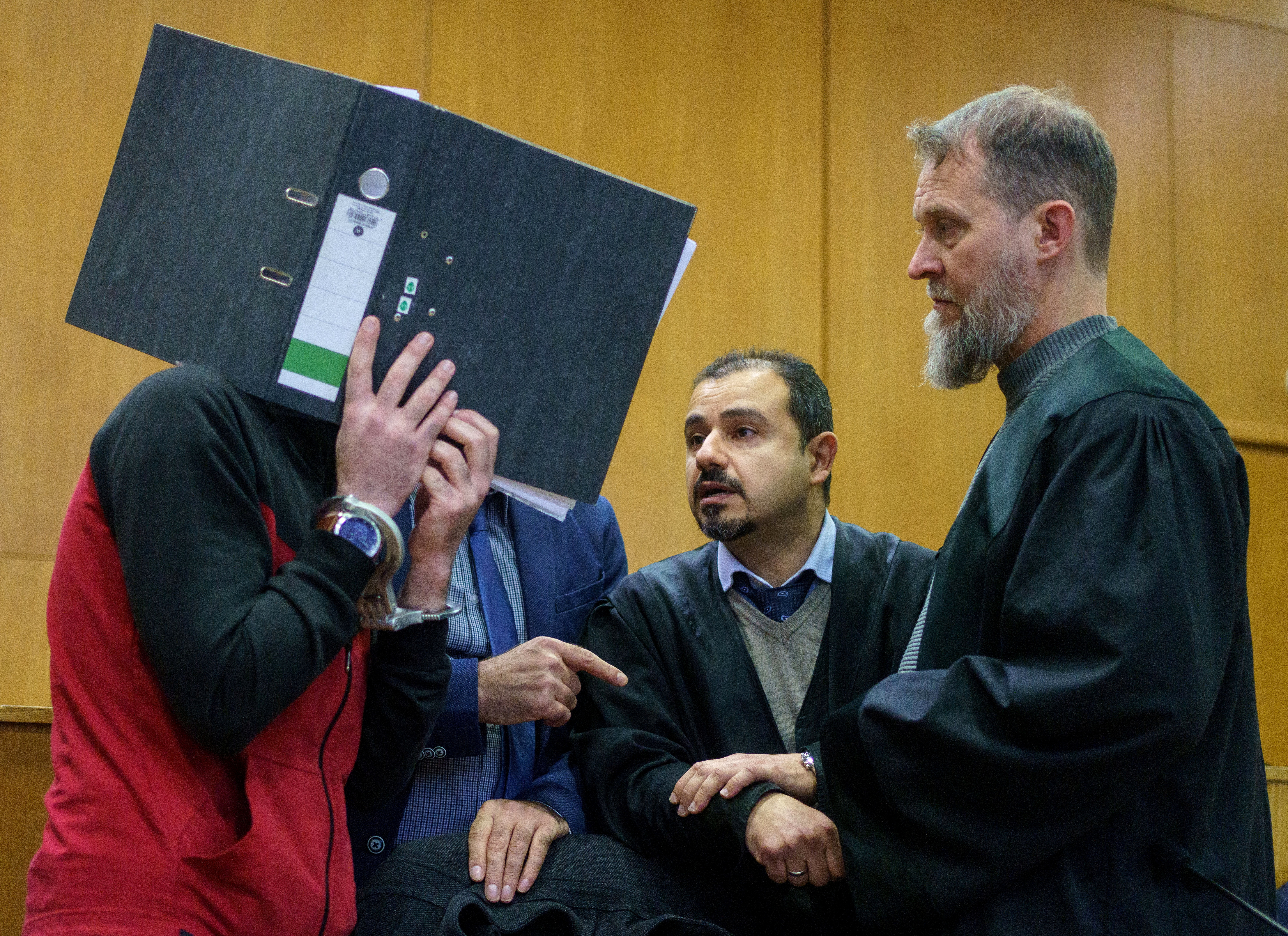 Iraqi defendant Taha Al-J. covers his face as he talks to his lawyers Serkan Alkan and Martin Heising before his verdict in a courtroom in Frankfurt, Germany, November 30, 2021.        Frank Rumpenhorst/Pool via REUTERS