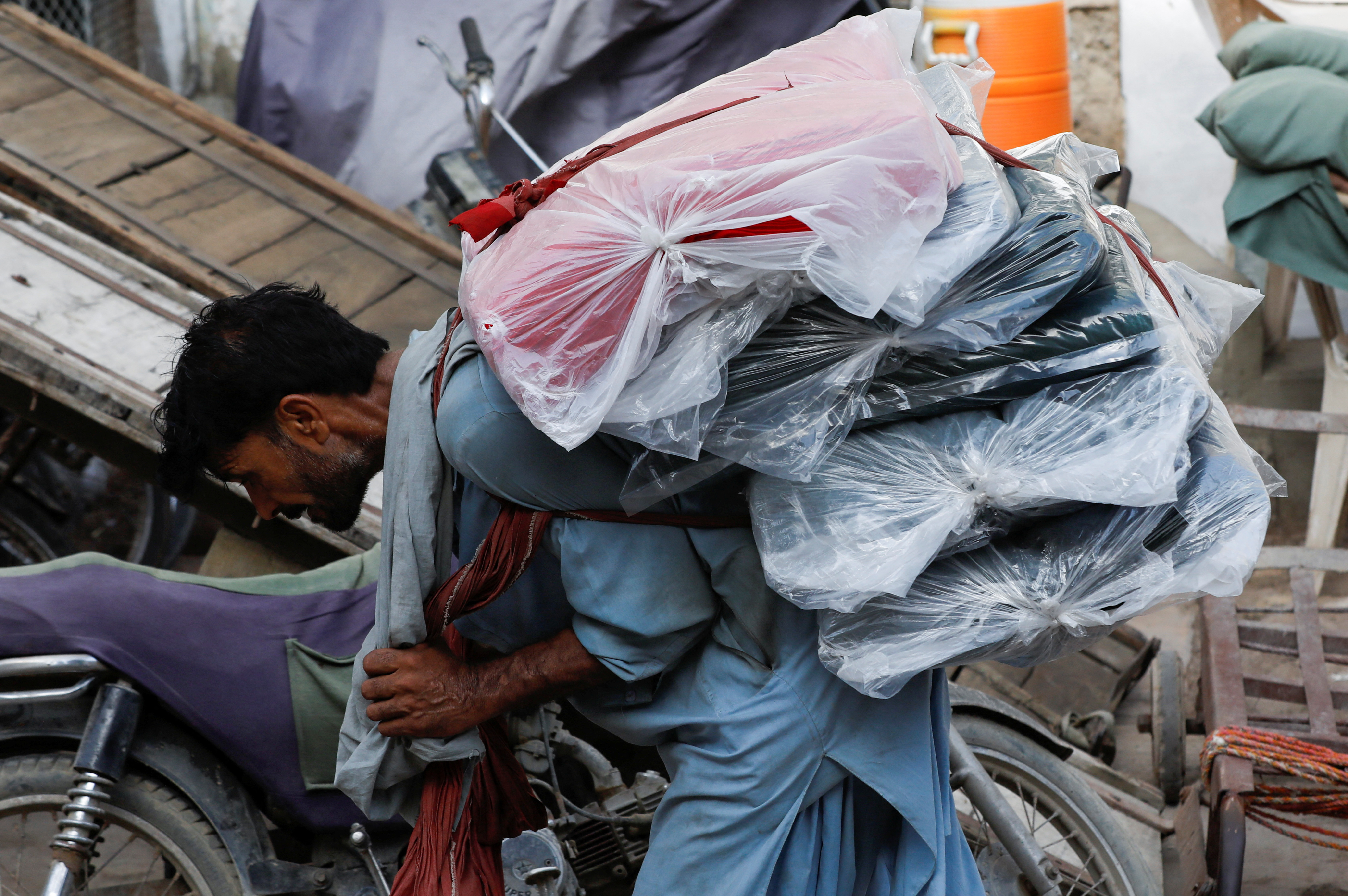 A labourer bends over as he carries packs of textile fabric on his back, in Karachi