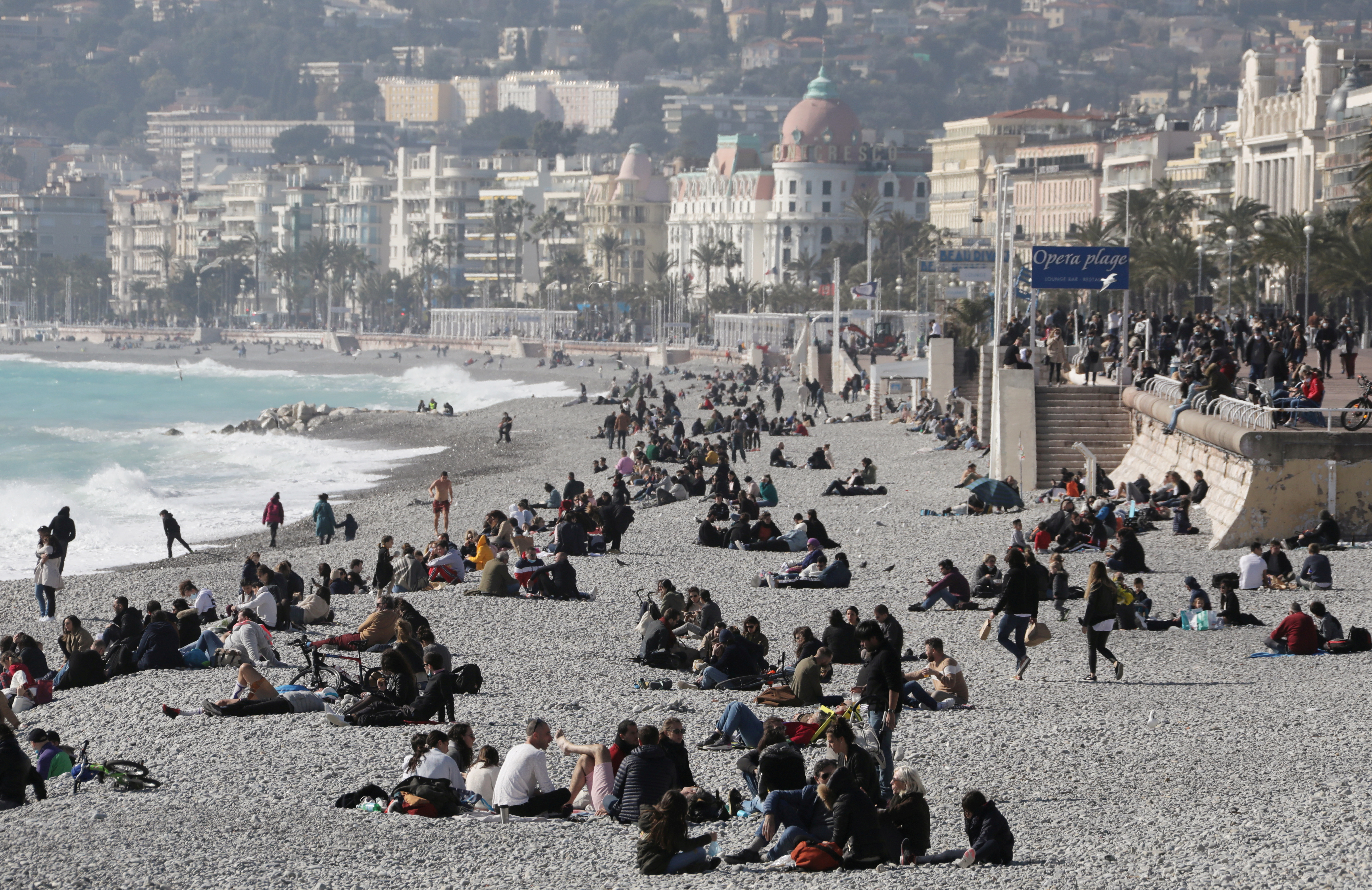 People sit on the beach of the Promenade des Anglais in Nice
