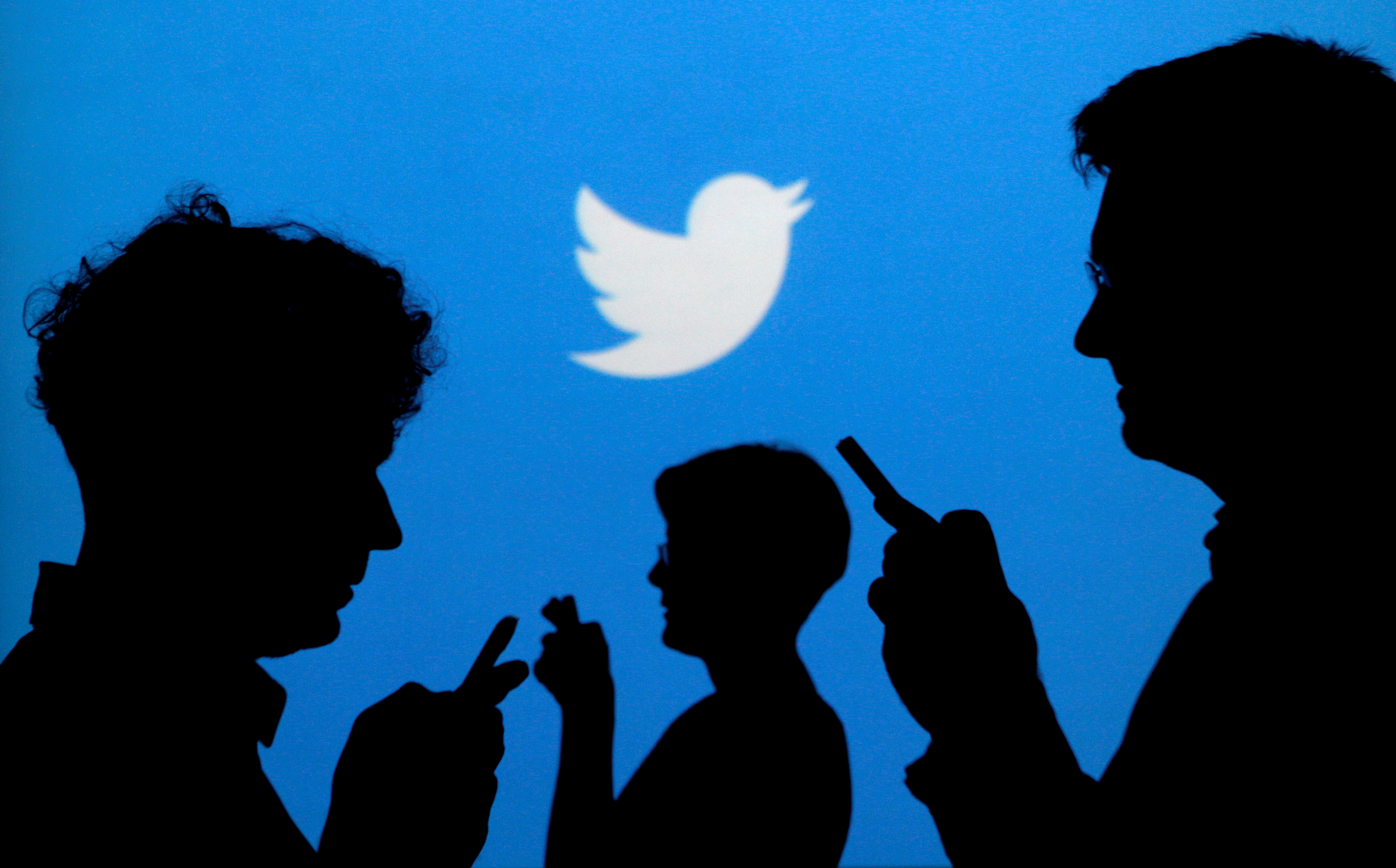 People holding mobile phones are silhouetted against a backdrop projected with the Twitter logo in this illustration picture taken September 27, 2013. REUTERS/Kacper Pempel/Illustration/File Photo