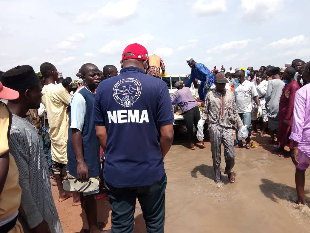 An official of the National Emergency Management Agency stands as people gather around a truck carrying bodies of the victims of a boat accident in Kebbi