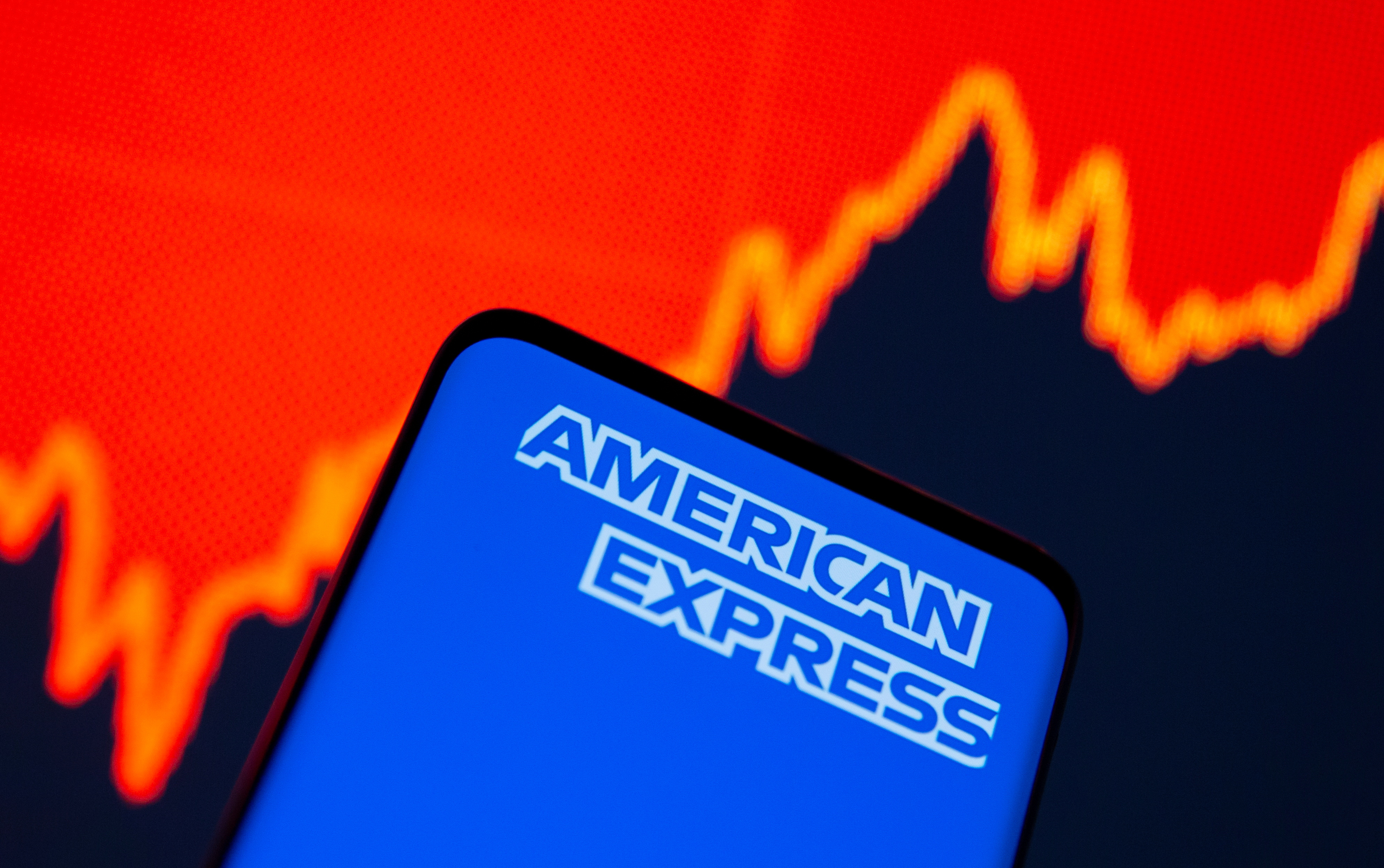 Smartphone with American Express logo is seen in front of displayed stock graph in this illustration