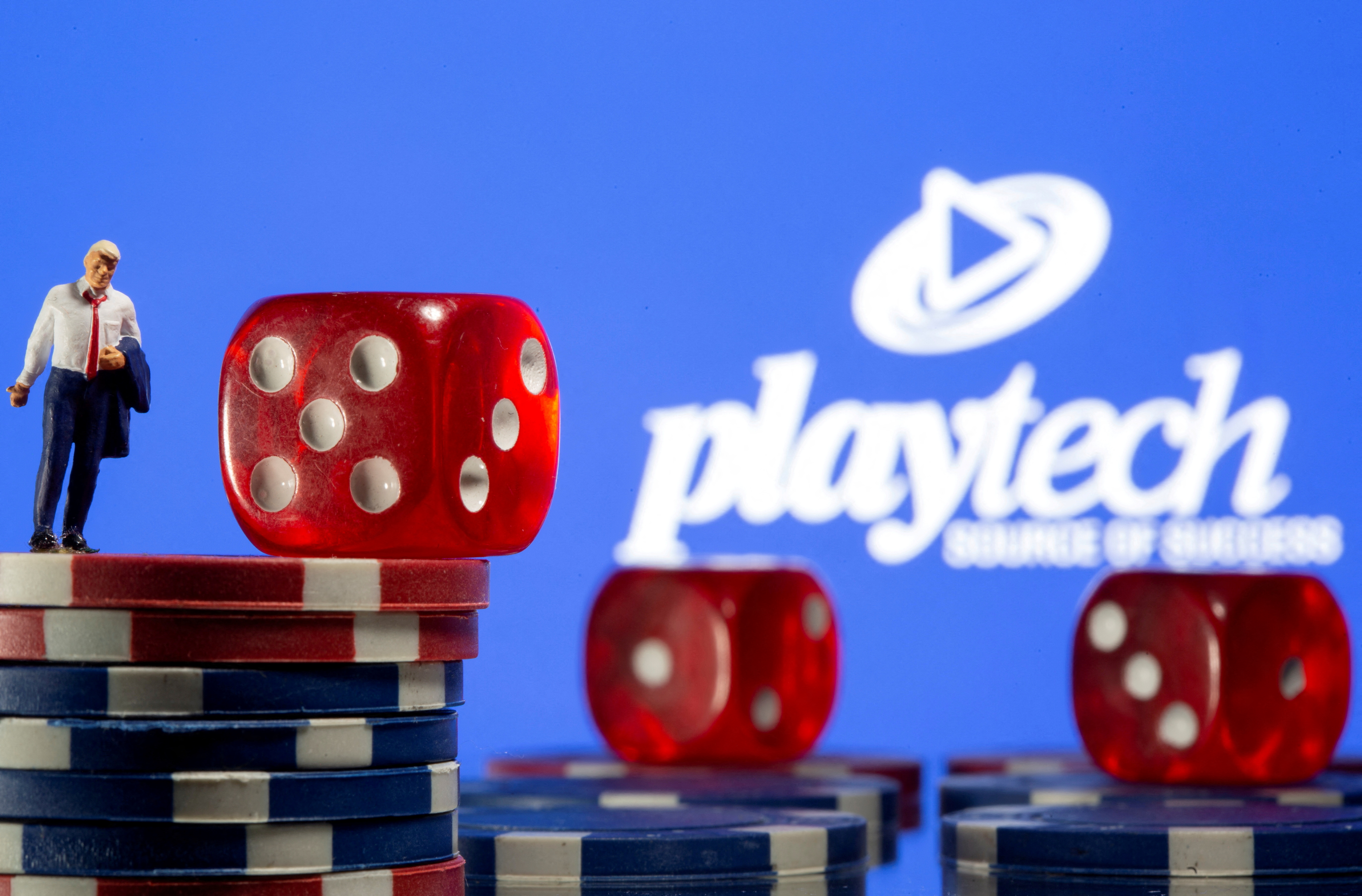 Businessman toy figure is placed on gambling chips in front of displayed Playtech logo in this illustration taken