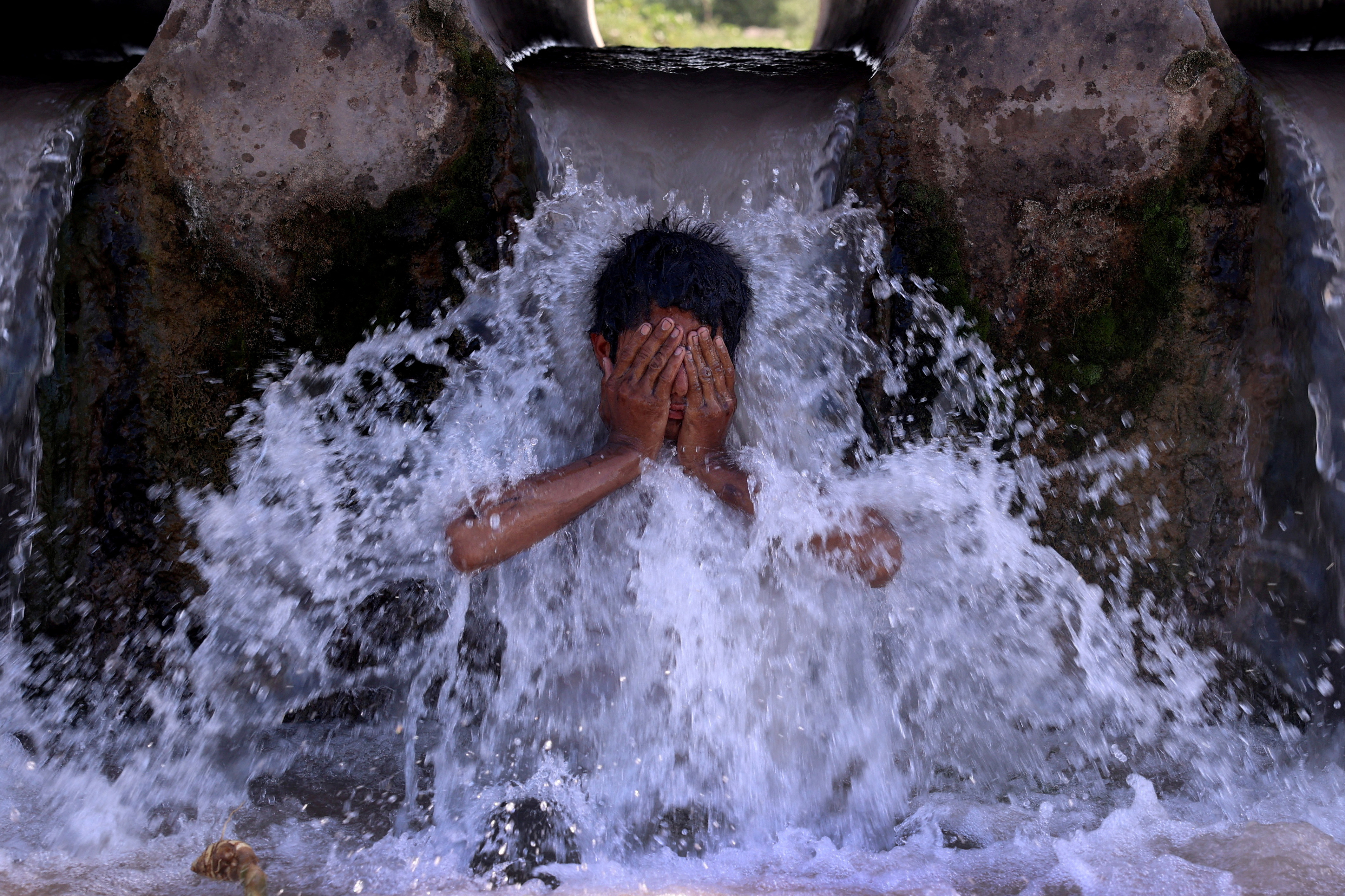 A boy cools off under a water pipe from a canal during a hot summer day on the outskirts of Peshawar