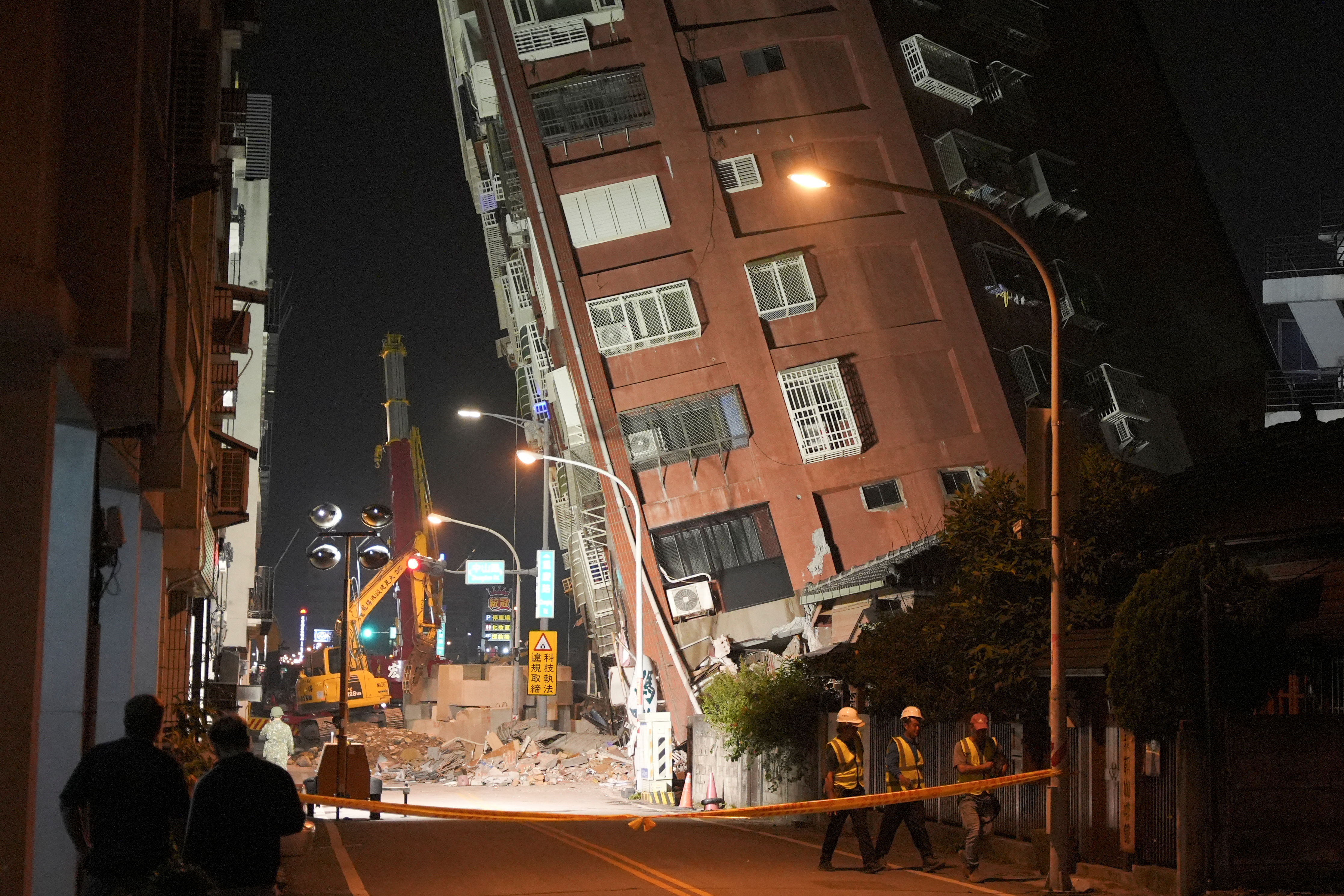 Hualien में उस स्थान पर चलते हुए श्रमिक जहां भूकंप के बाद एक इमारत ढह गई थी