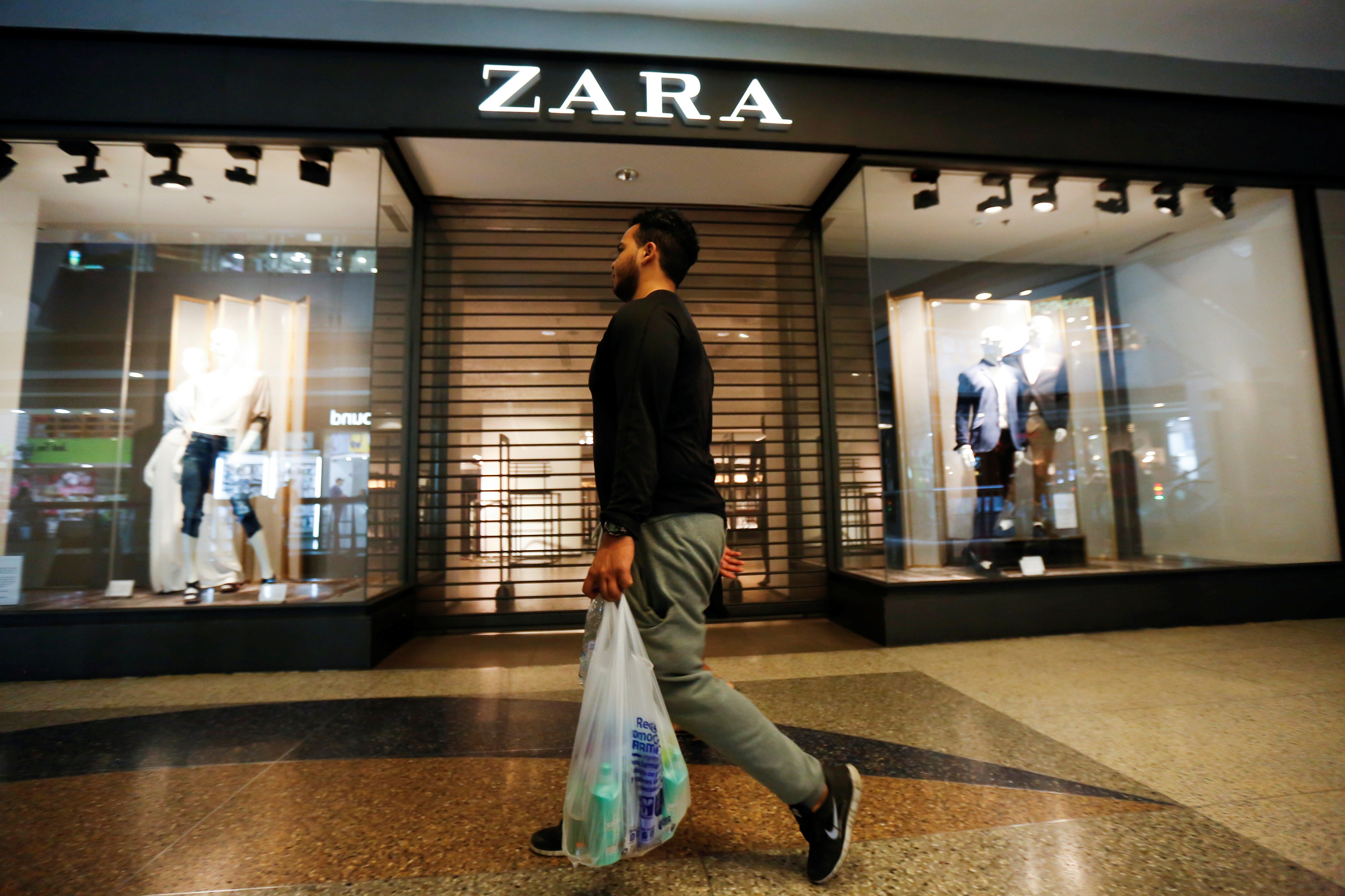 A man walks past a Zara retail store, with its shutters drawn, at a mall in Caracas