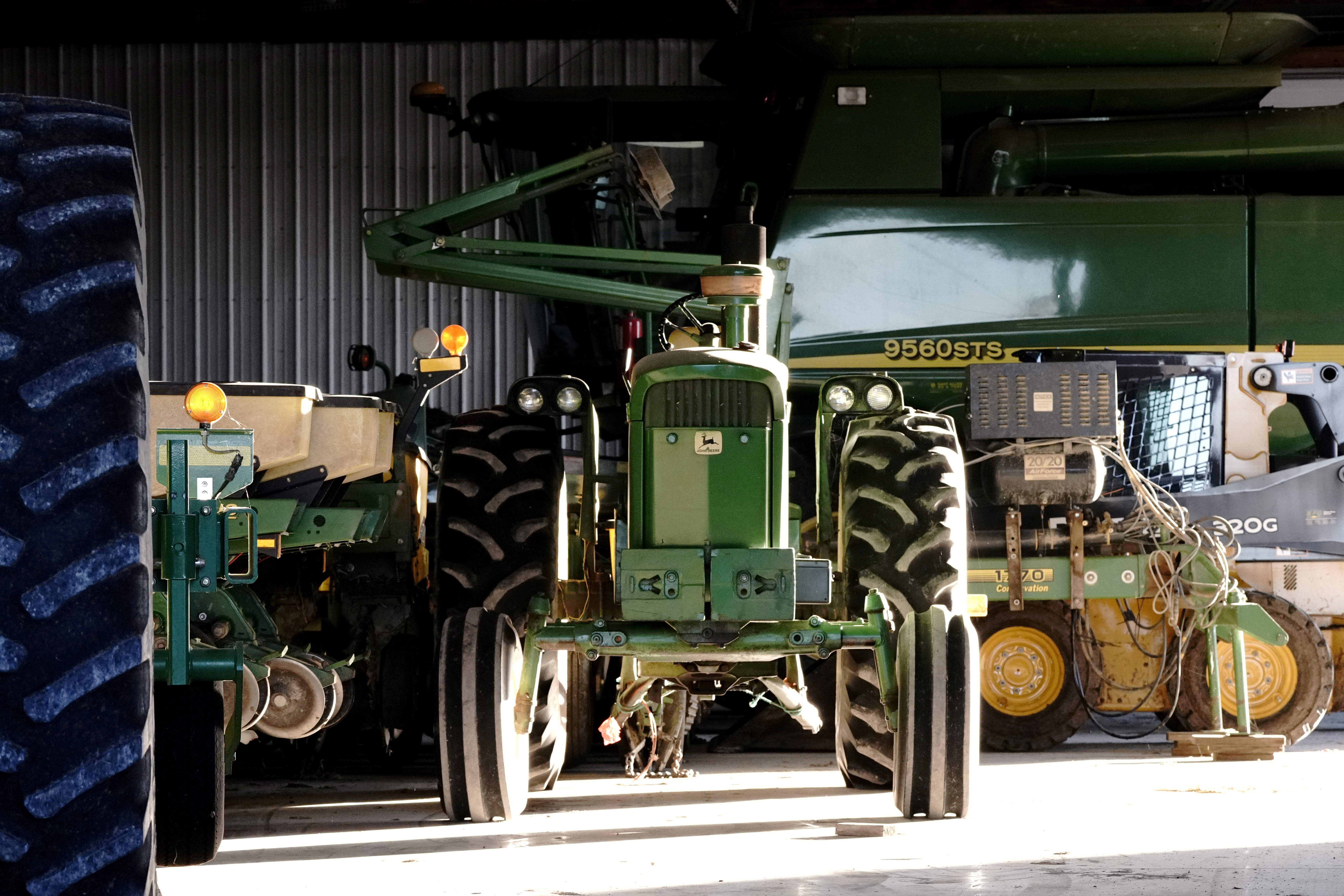 A John Deere tractor, a combine, and other heavy machinery sit inside a barn on a corn and soybean farm in Woodburn, Indiana