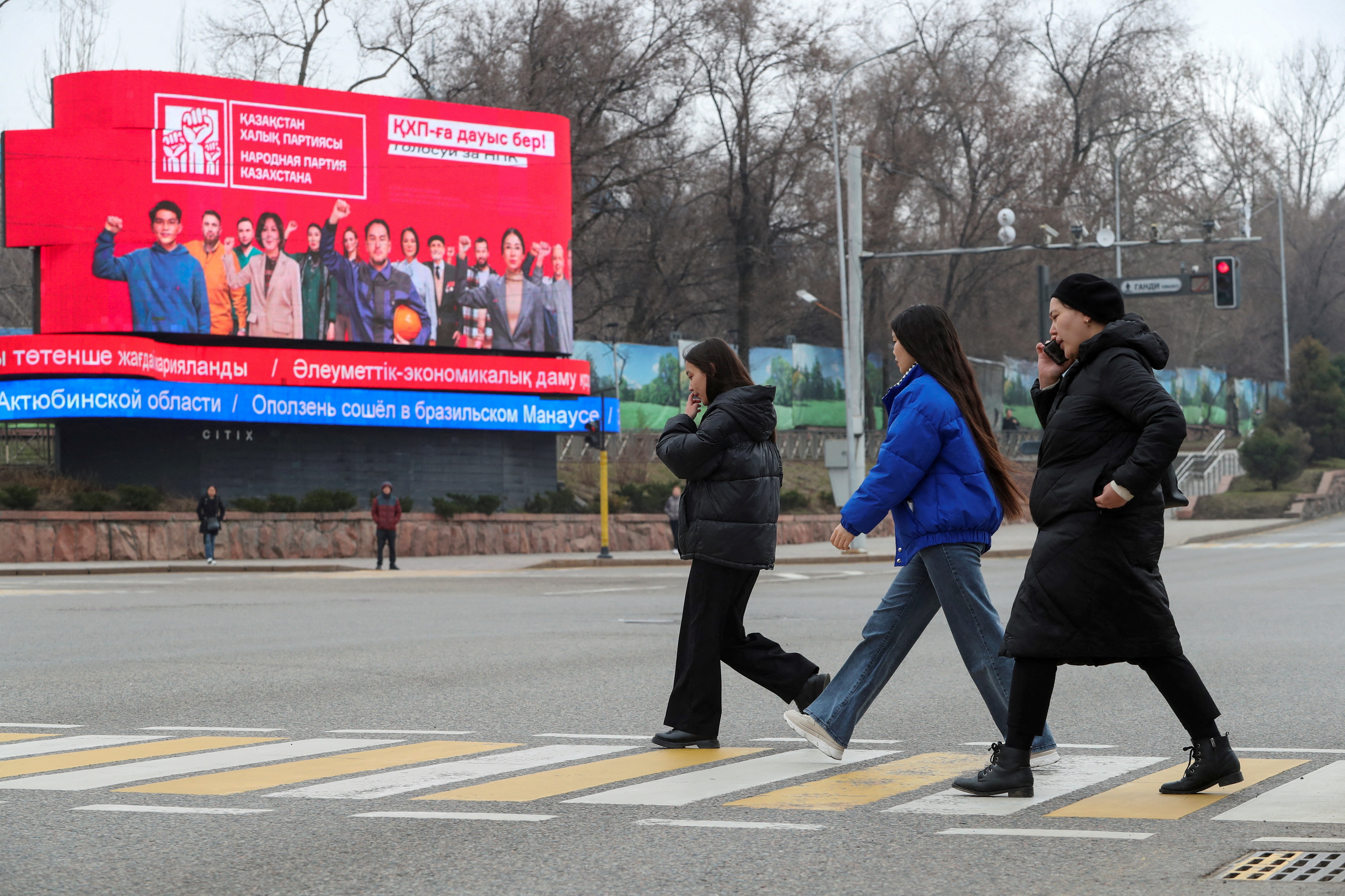 Pedestrians cross a road near a parliamentary elections campaign board in Almaty