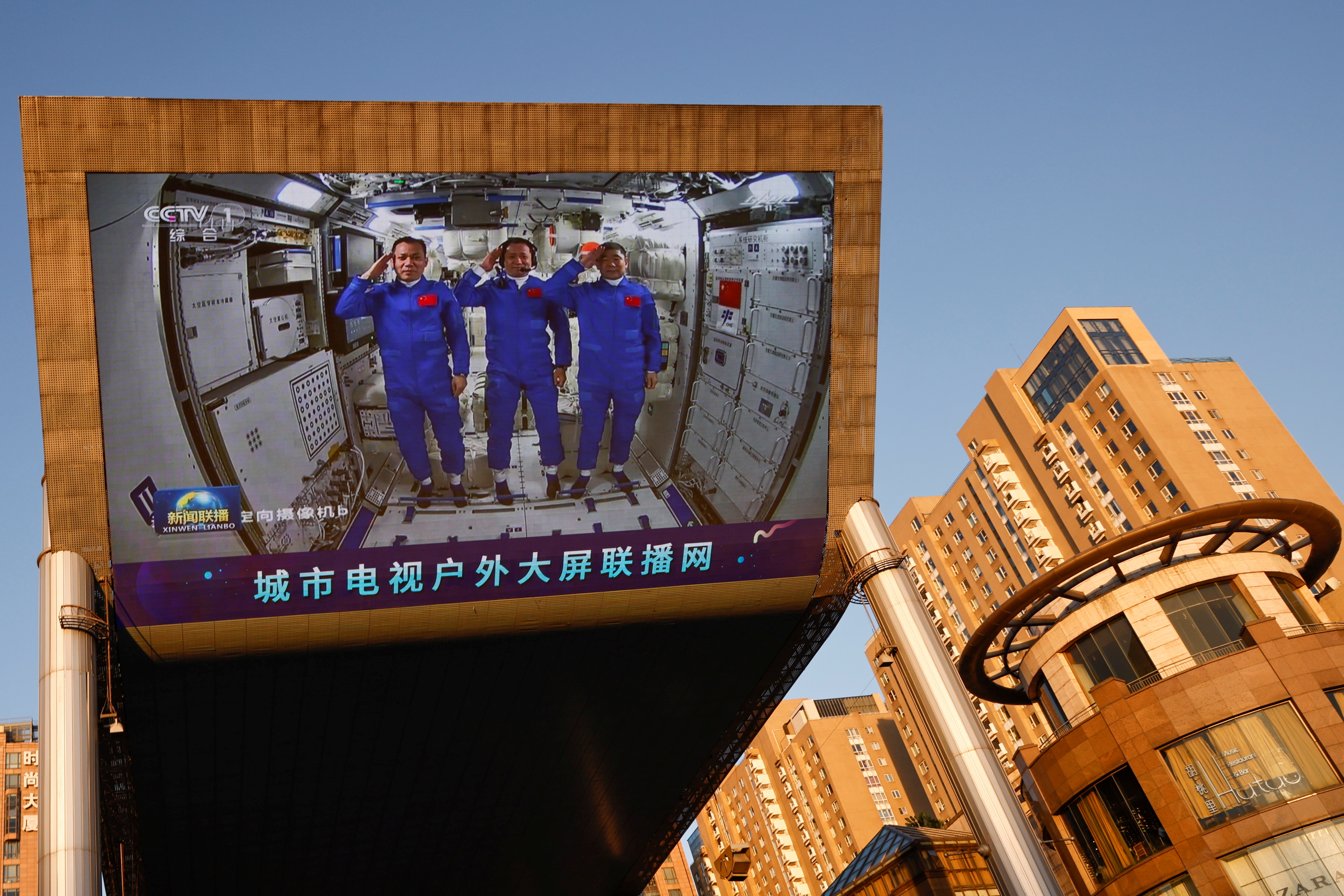 A giant screen shows Chinese astronauts Nie Haisheng (C), Liu Boming (R), and Tang Hongbo of the Shenzhou-12 mission saluting inside the Tianhe core module of China's space station, at a shopping mall in Beijing, China June 18, 2021. REUTERS/Thomas Peter