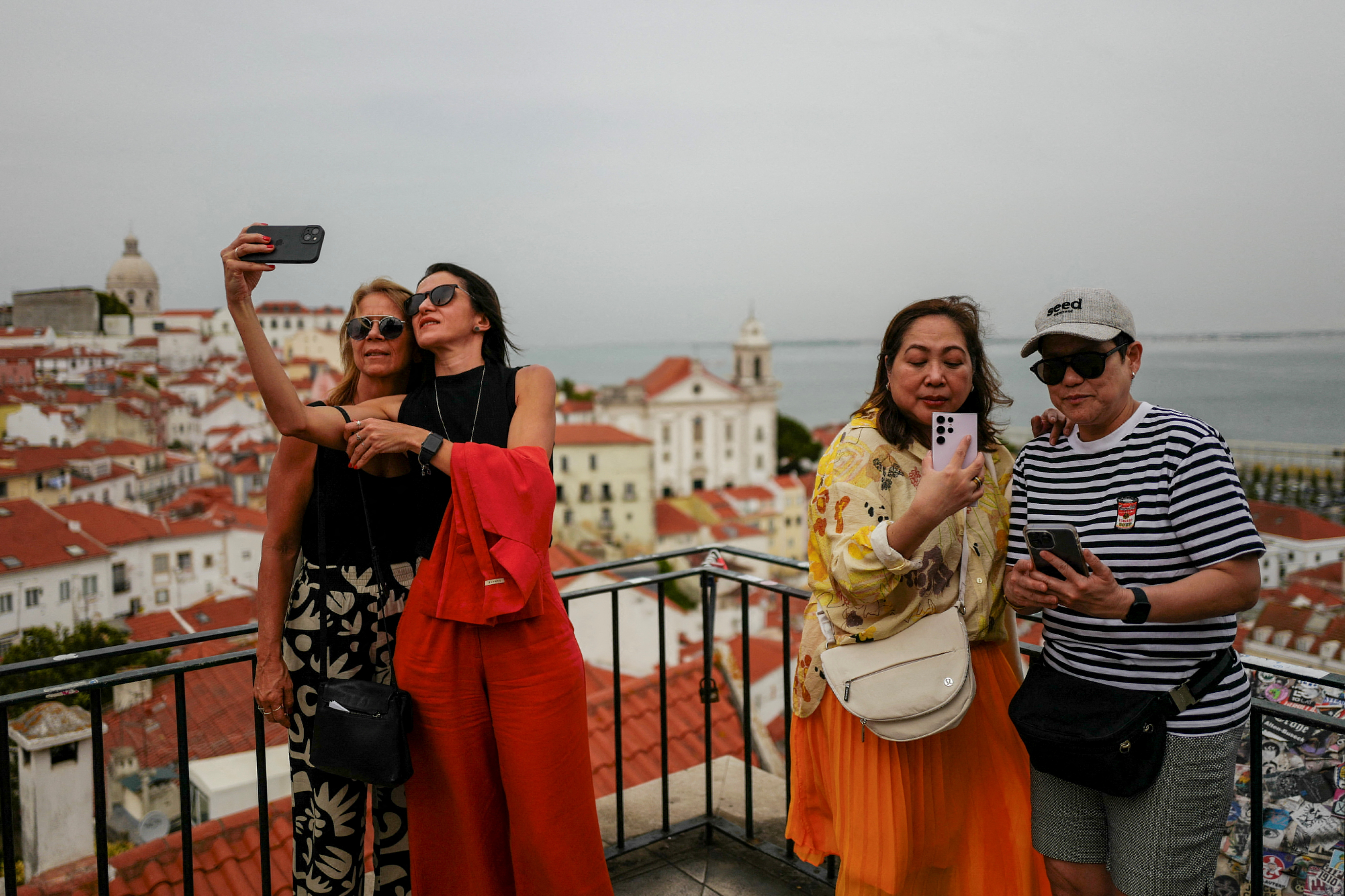 People take pictures from a viewpoint in Alfama neighbourhood in Lisbon