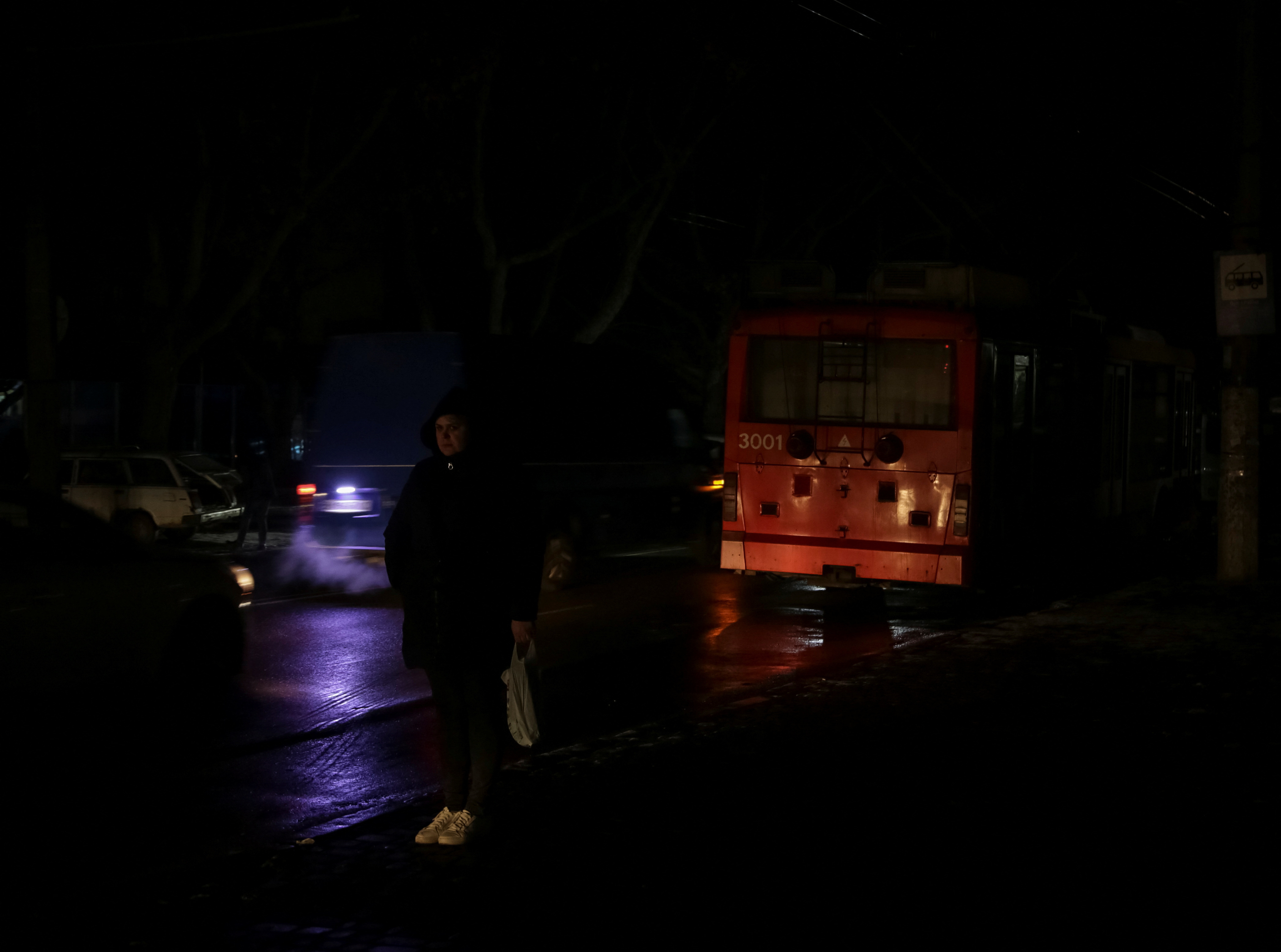 A local resident stands at a transport stop near a stopped trolleybus during a power outage after critical civil infrastructure was hit by Russian missile attacks in Odesa