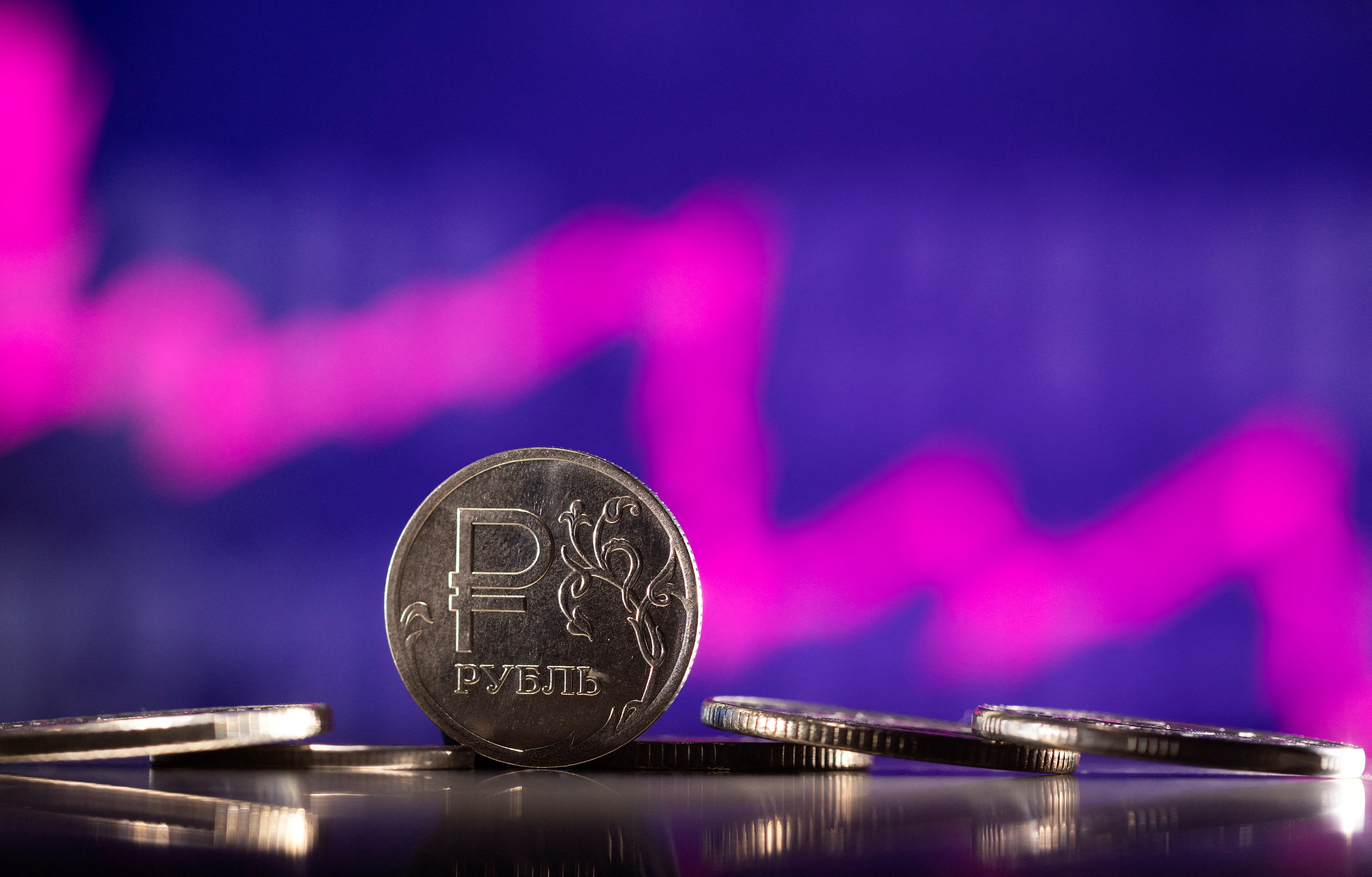 Illustration shows Russian Rouble coins are seen in front of descending stock graph