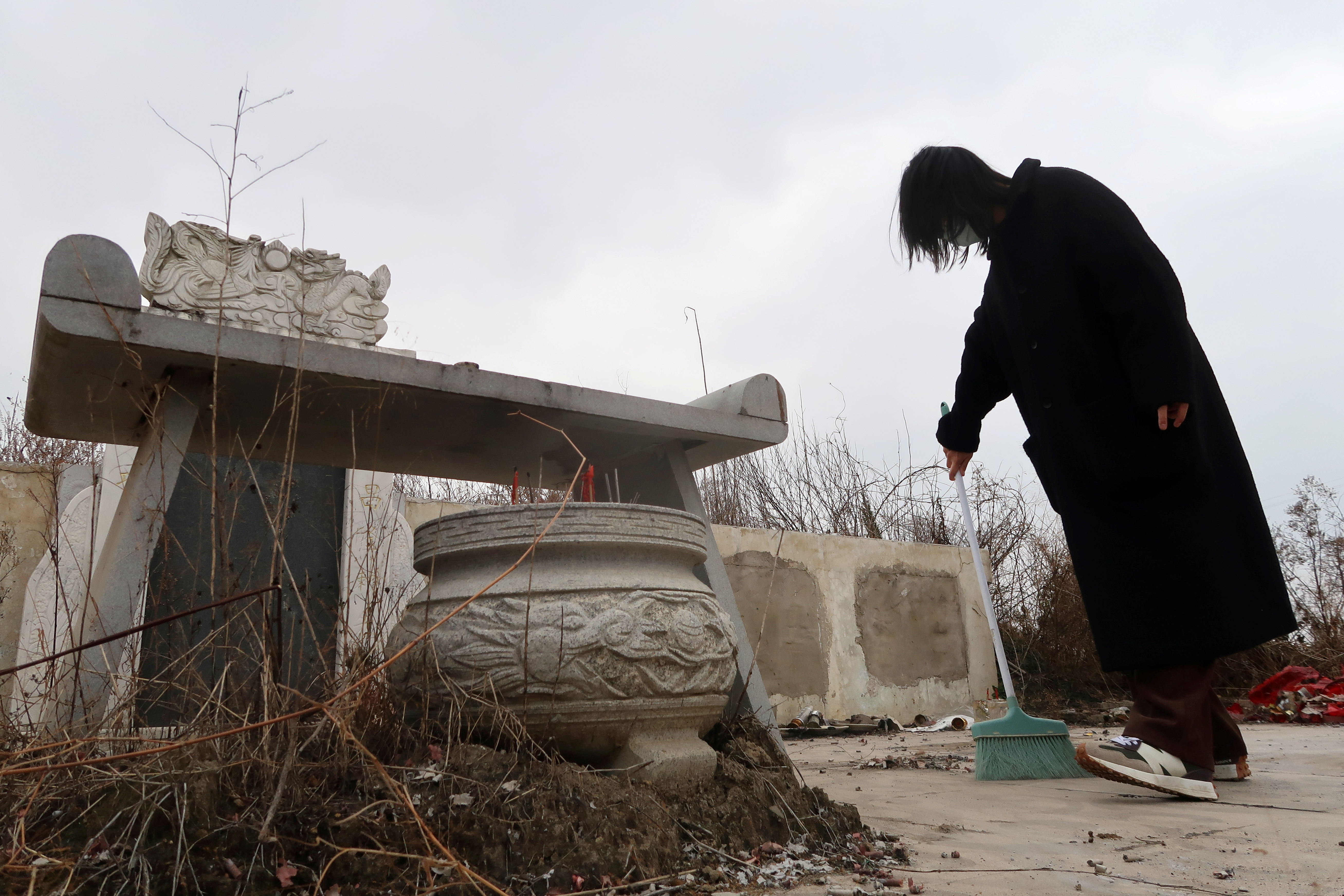 Deng Wei sweeps in front of her grandmother's and father's tombs in Wuhan