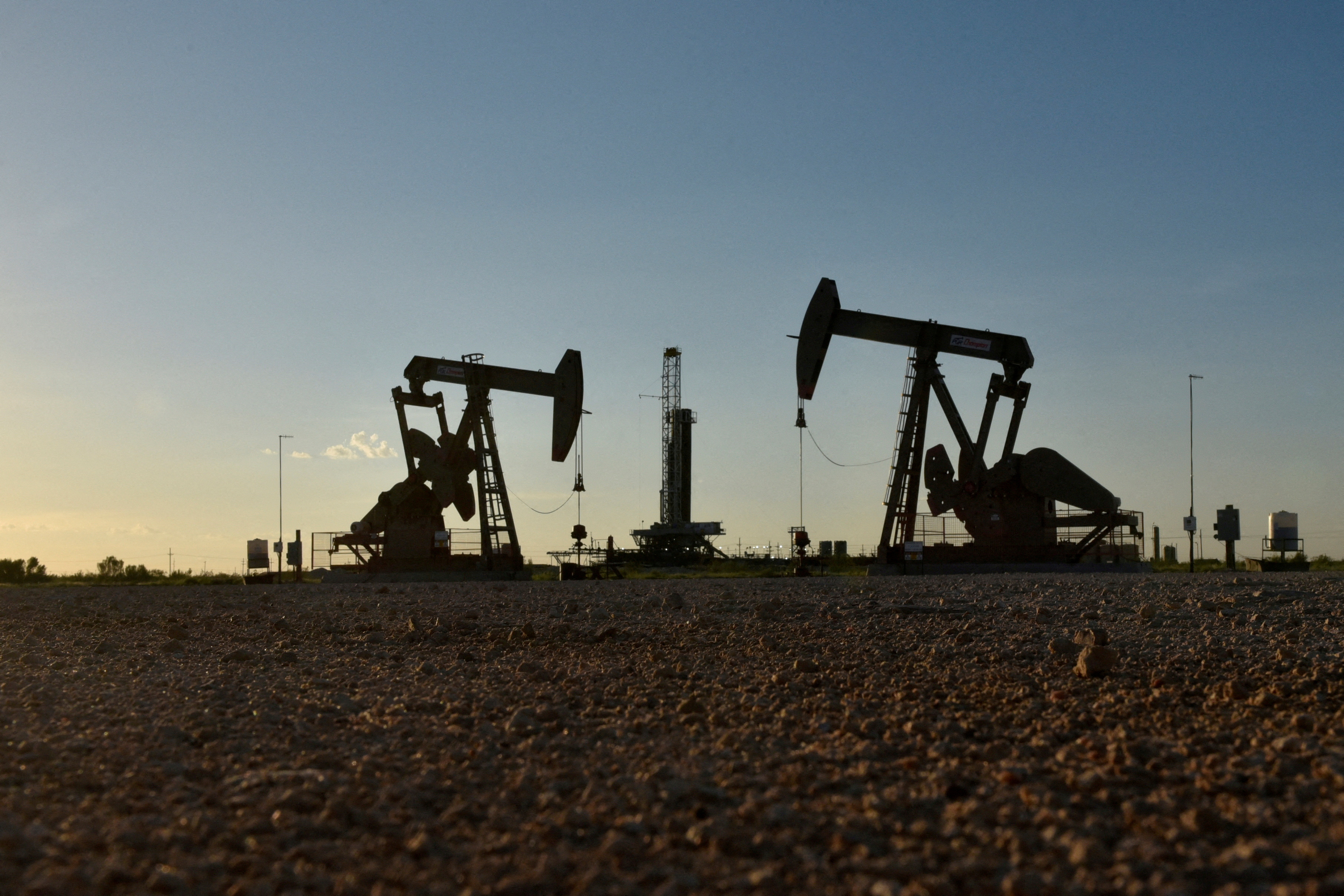 Pump jacks operate in front of a drilling rig in an oil field in Midland
