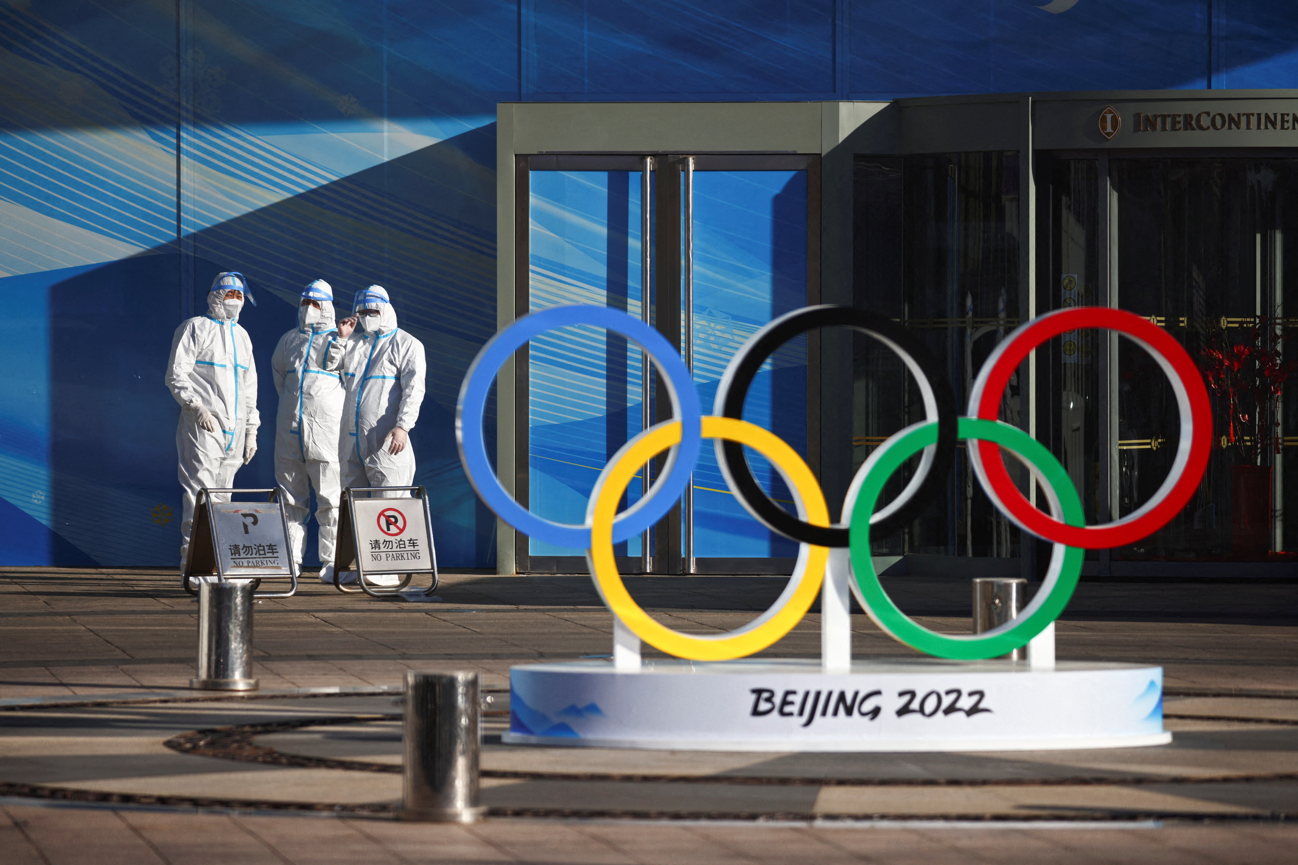 Workers in PPE stand next to the Olympic rings inside the closed loop area near the National Stadium in Beijing