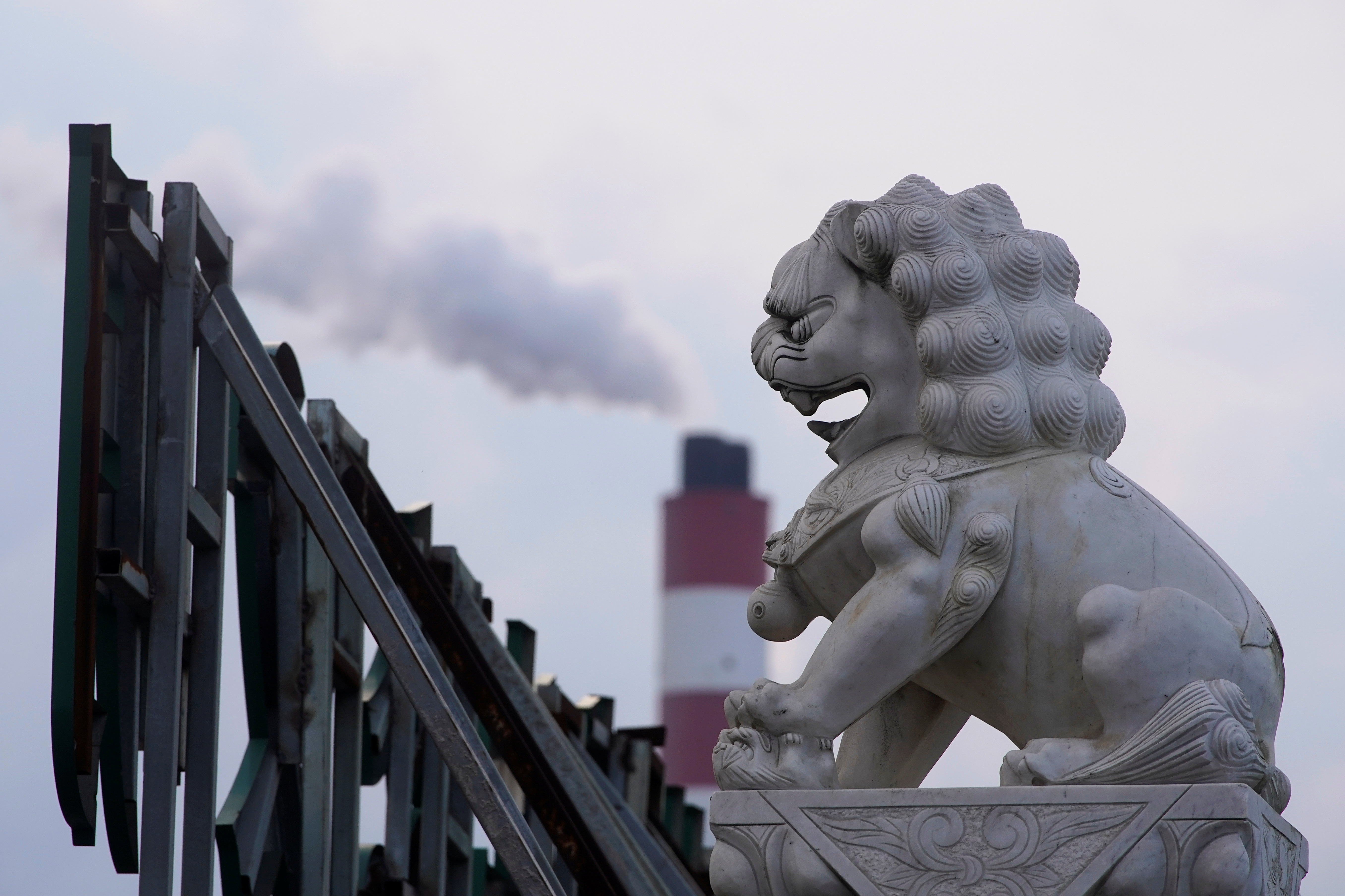 Chimney of a coal-fired power plant stands behind a lion statue in Shanghai