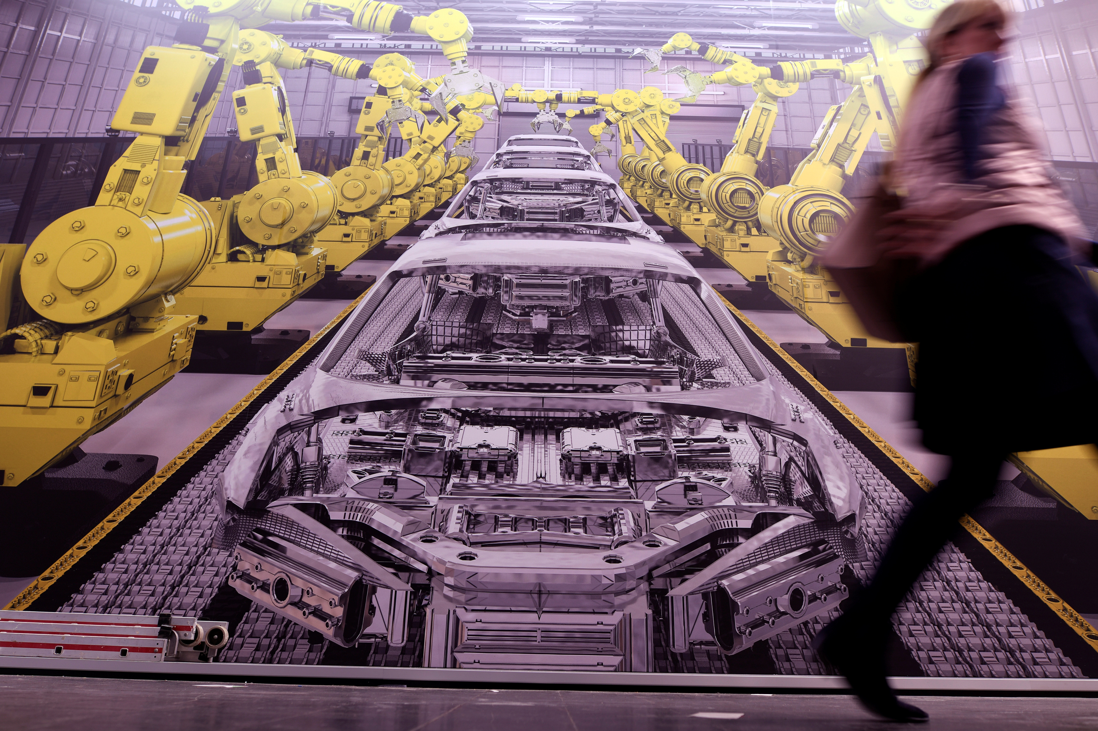 A woman passes a poster showing a production line with robots at the Hanover trade fair, in Hanover