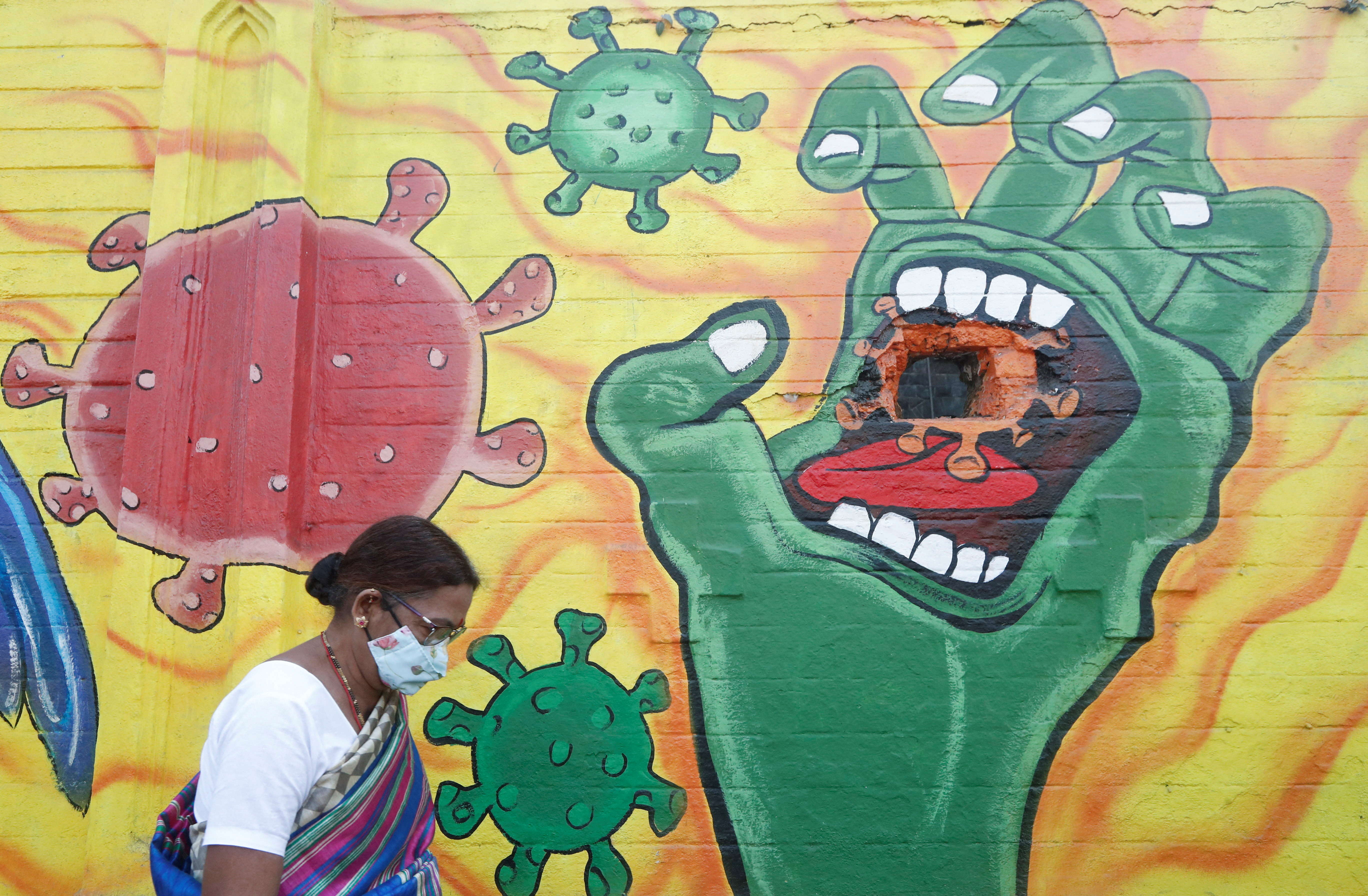 A woman wearing a protective face mask walks past a mural on a street, amidst the spread of COVID-19, in Mumbai