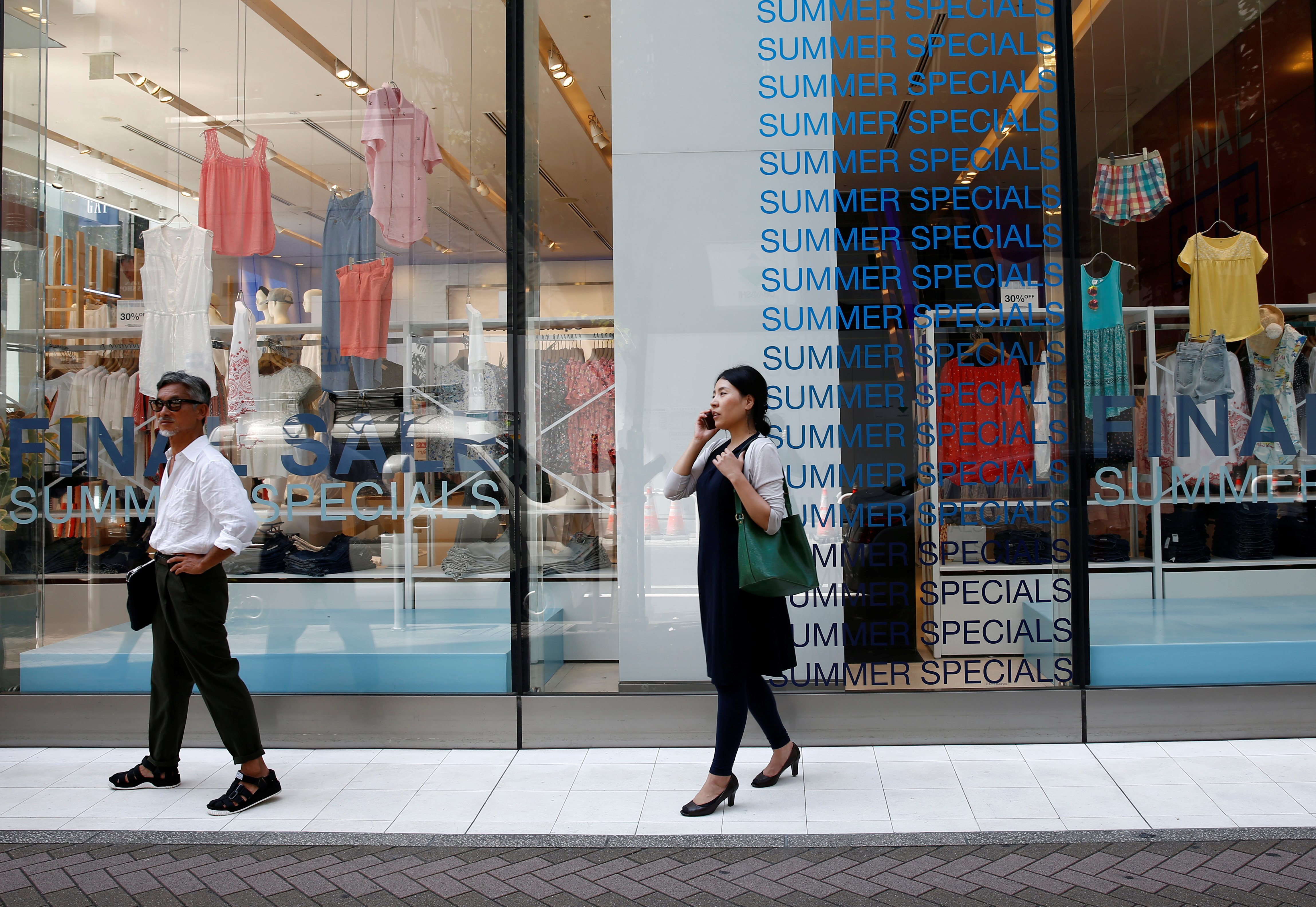 Pedestrians stand in front of sale signs on a shopfront at a shopping district in Tokyo