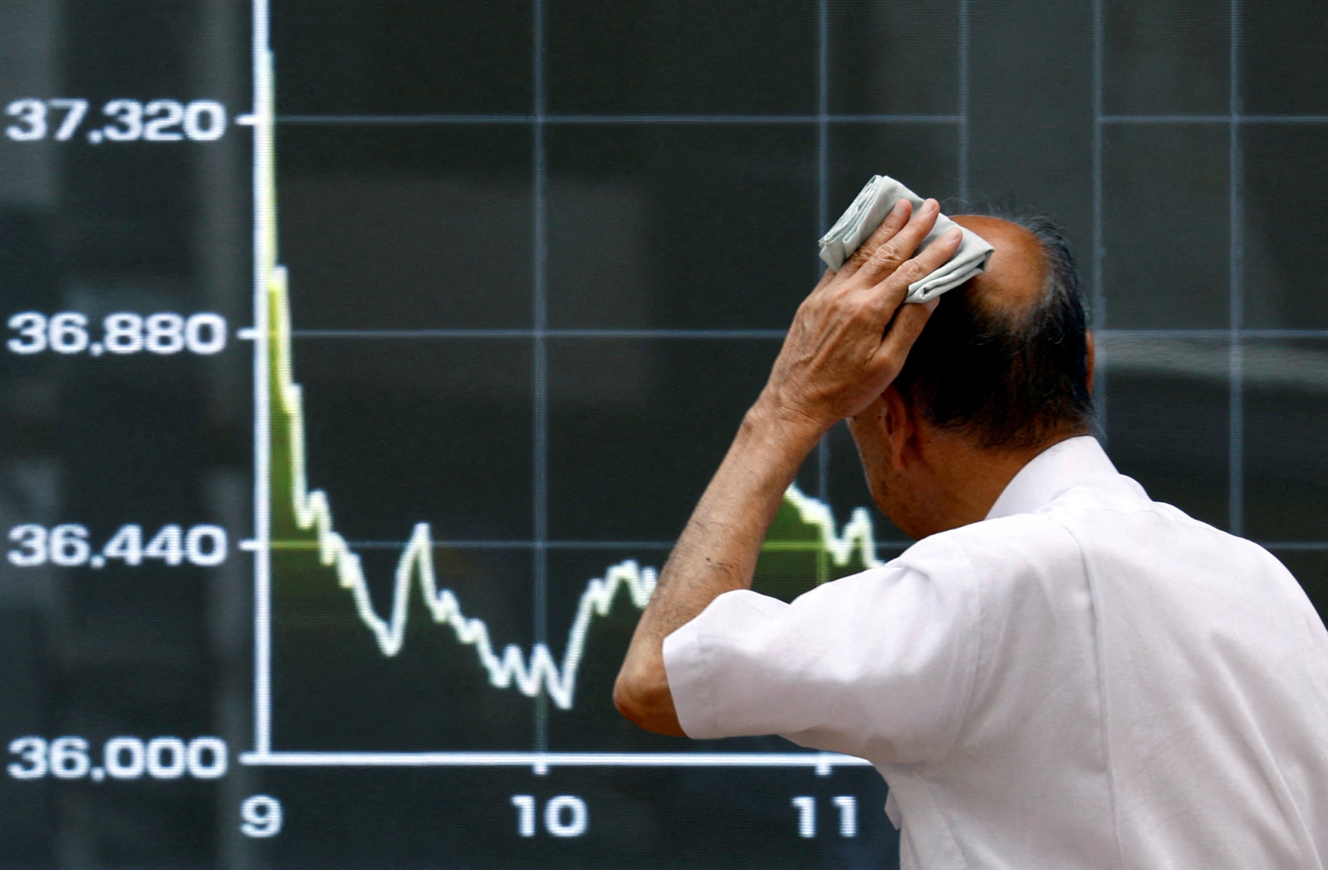 A passerby walks past in front of an electronic screen displaying the graph showing today's movements of Japan's Nikkei share average in Tokyo